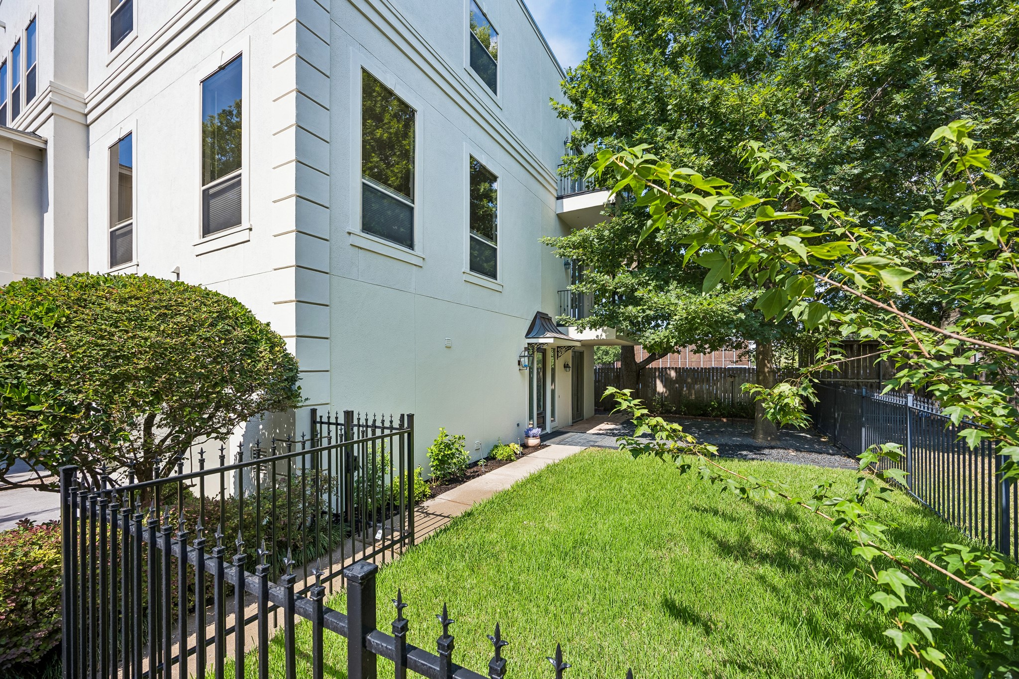 Rare private grass yard framed by an iron fence and shaded by established landscaping.