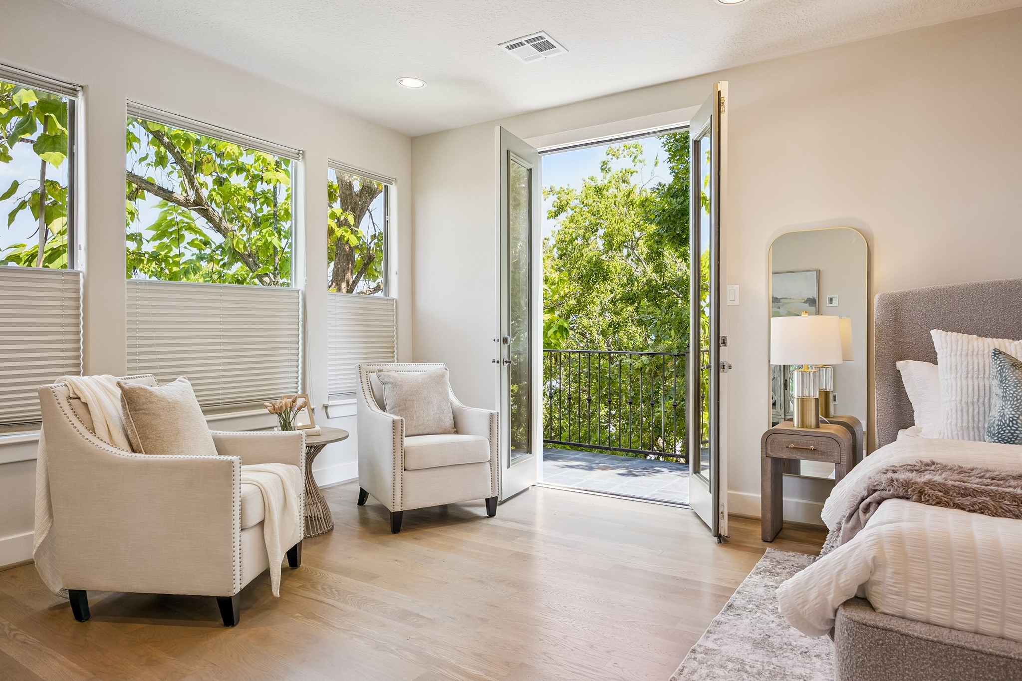 Primary suite with French doors opening to a private balcony surrounded by mature trees.