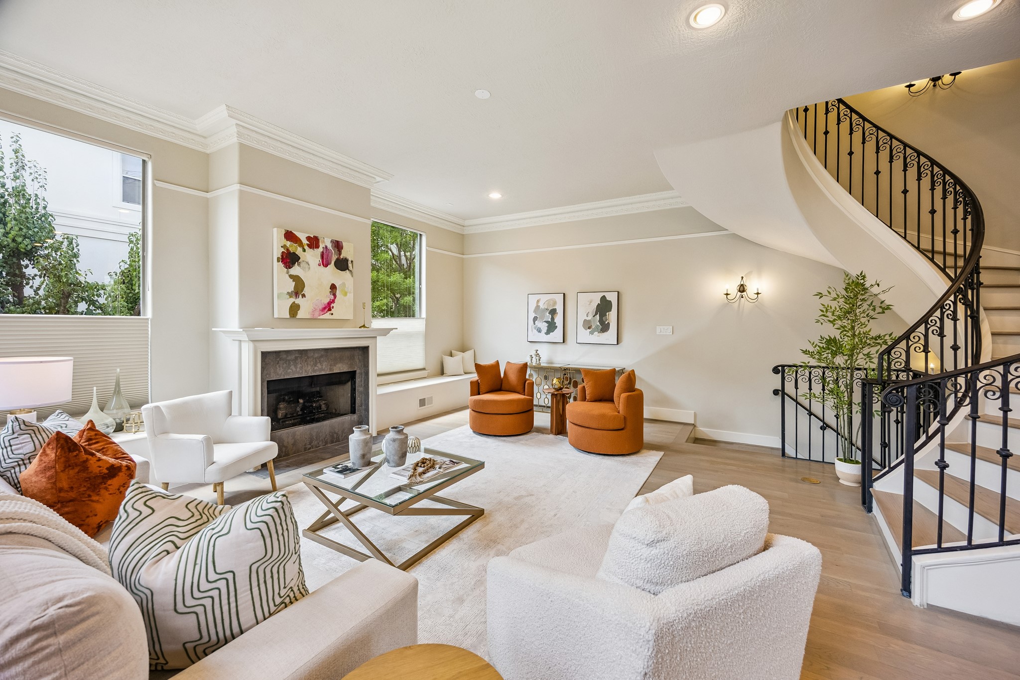 Generously proportioned living room with hardwood floors, high ceilings and windows on multiple sides, complemented by a dramatic curved staircase and an open, airy layout.
