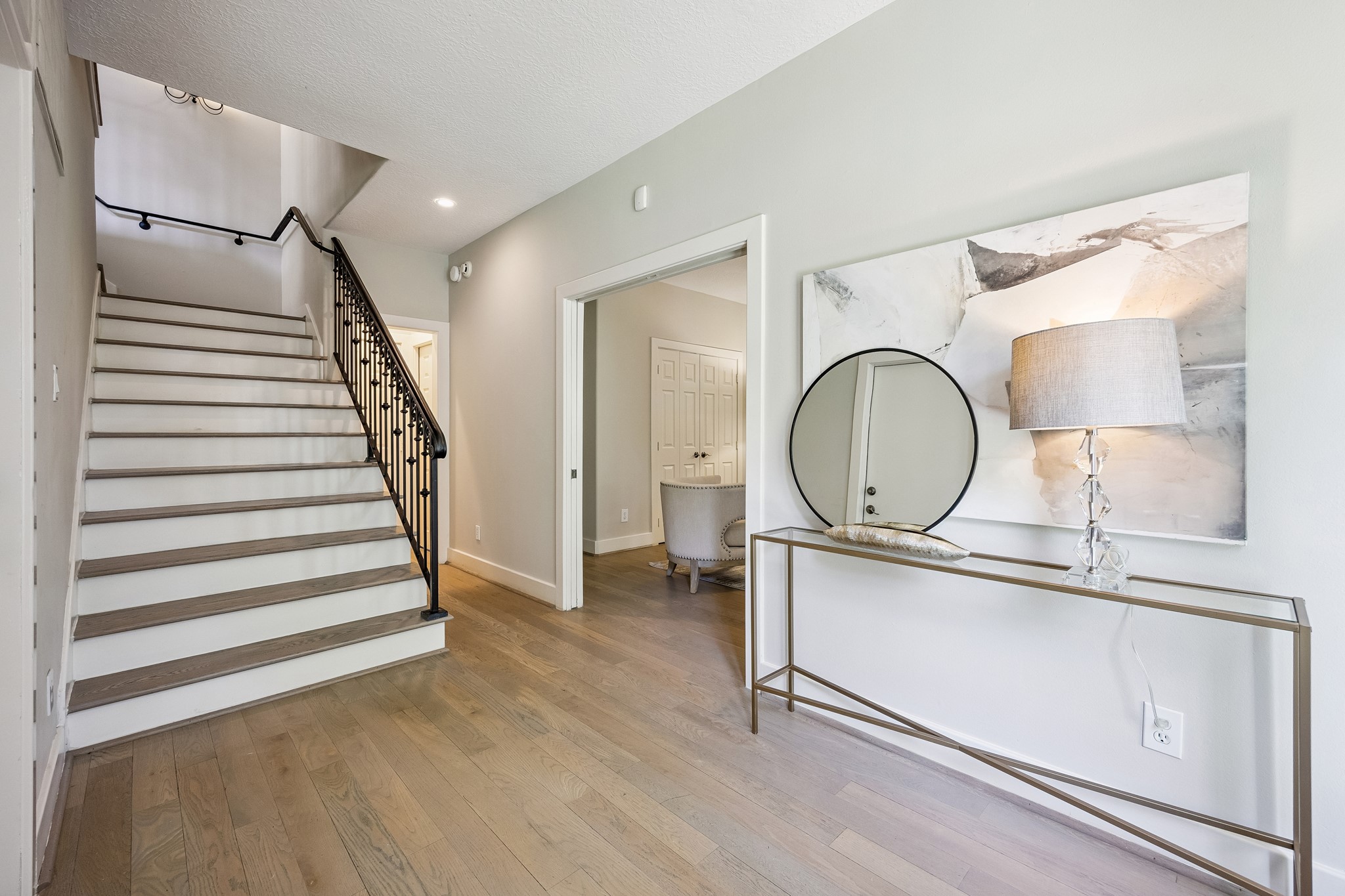 Light-filled entry hall with hardwood flooring and a curved staircase accented by an iron banister. Wood flooring continues throughout all living areas and bedrooms (no carpet).