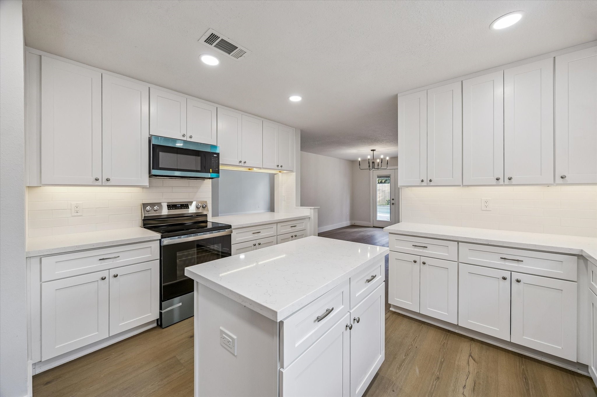 Kitchen continuation showcasing Carrara quartz island and perimeter countertops, new cabinetry with updated hardware, new stainless appliances, and white oak LVP flooring. Every detail is new.