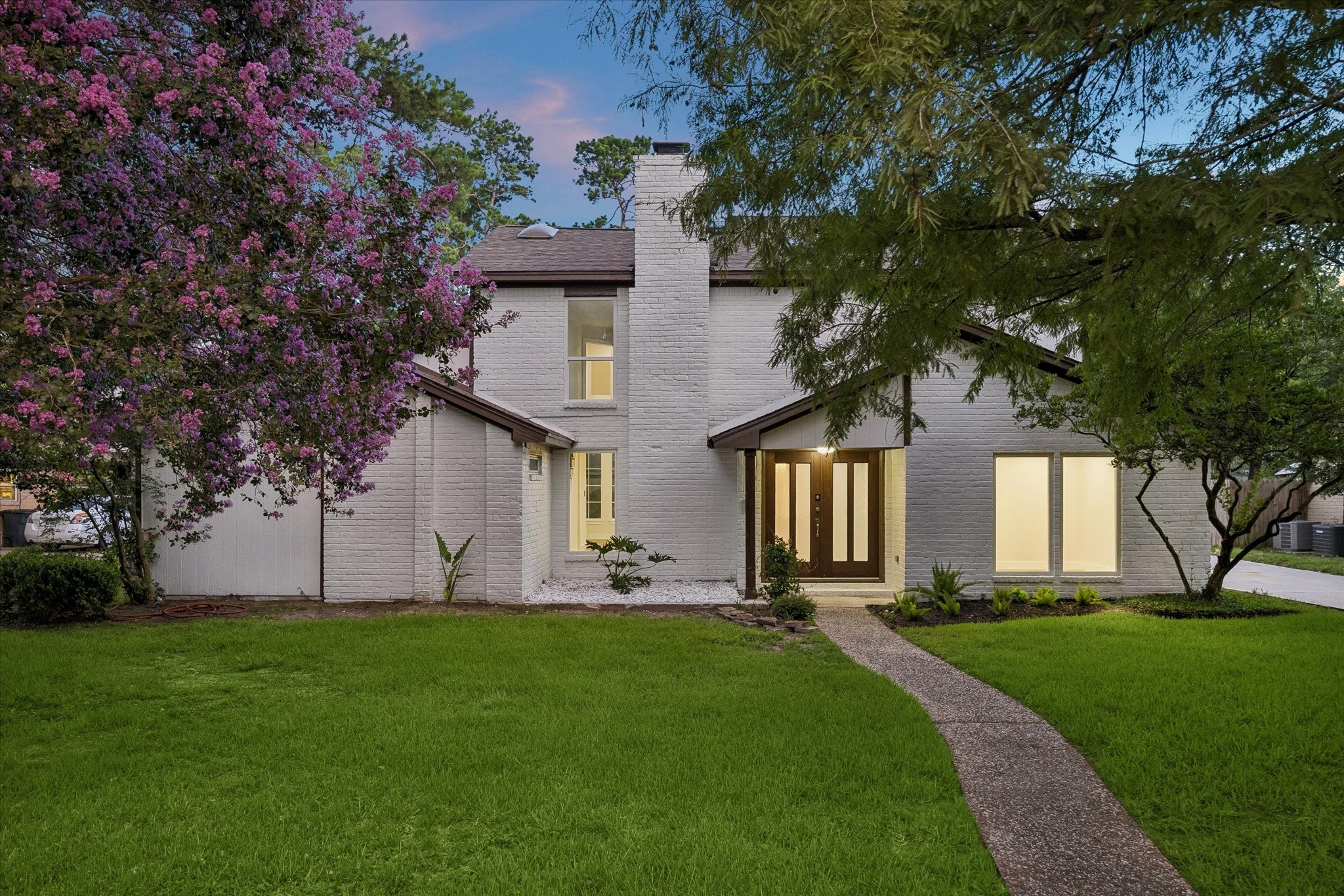 Freshly painted original brick elevation showcasing a fully renovated home with new 30-year architectural shingle roof, new windows, and new exterior doors. Lush manicured lawn with mature trees and updated curb appeal.
