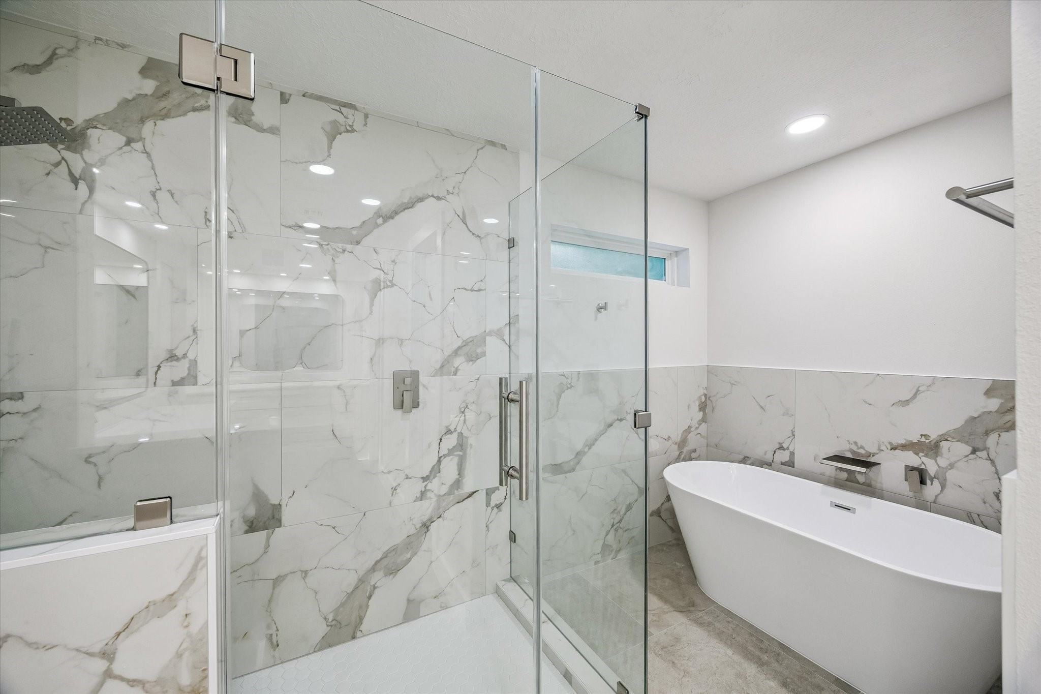 Master bathroom reimagined with large-porcelain tile, frameless shower enclosure, large soaking tub, w. waterfall faucet head, chrome finishes.