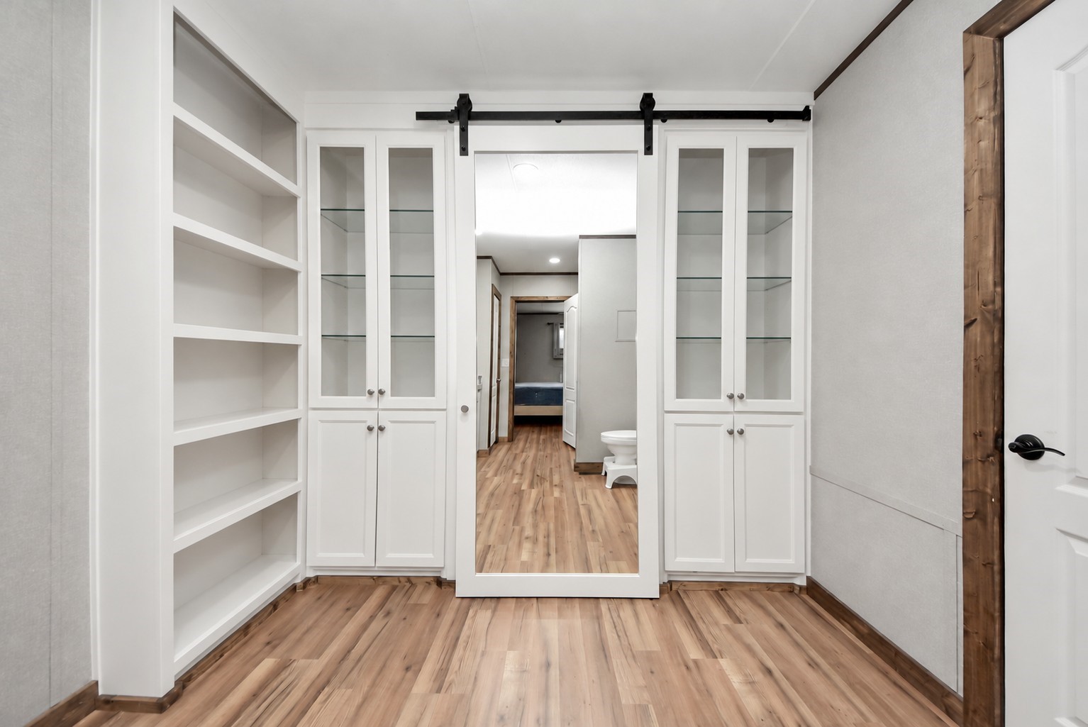 Bathroom built-in shelving and glass-front storage cabinets with sliding mirrored barn door.