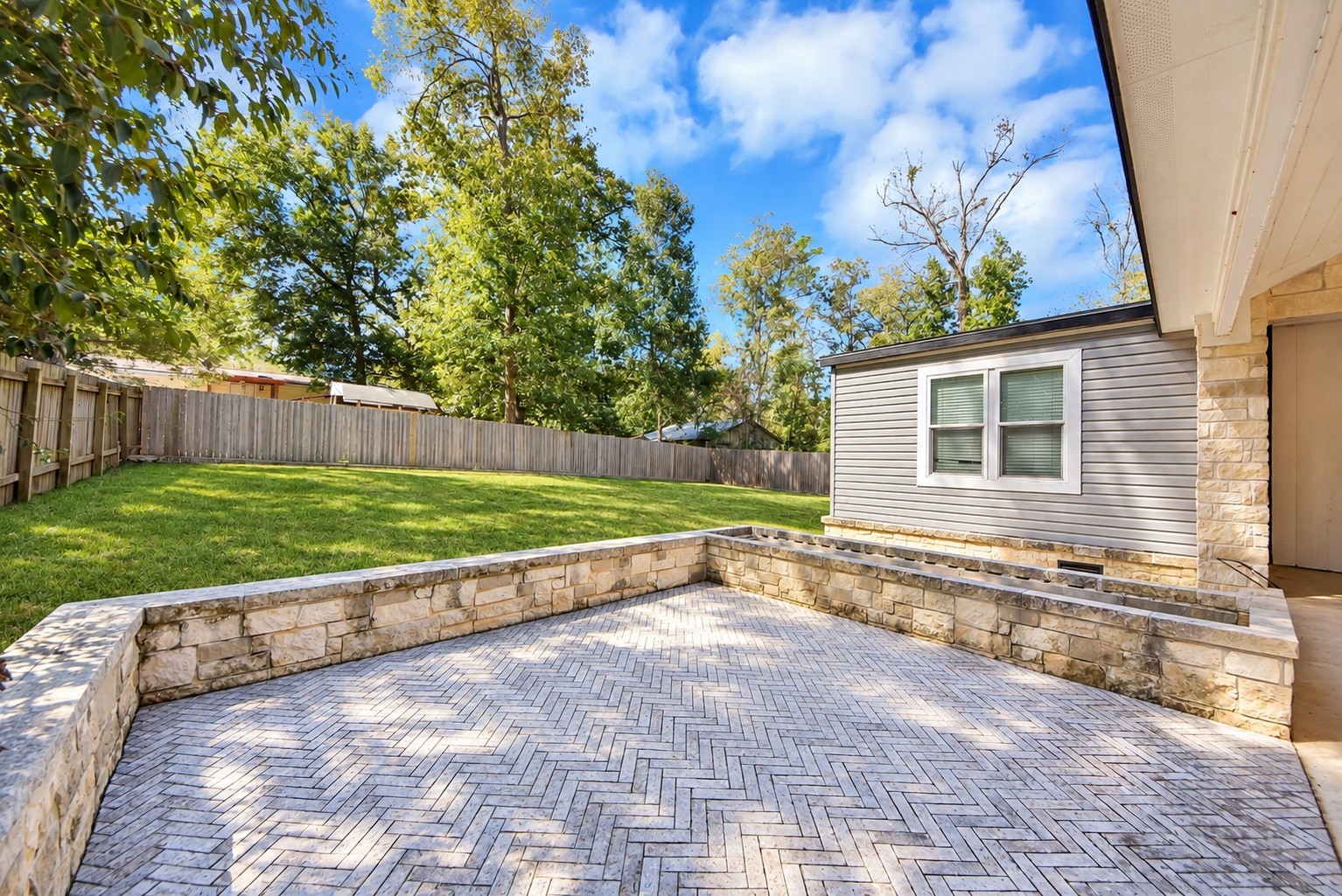 Spacious open-air patio with stone pavers, directly connecting to the expansive backyard.