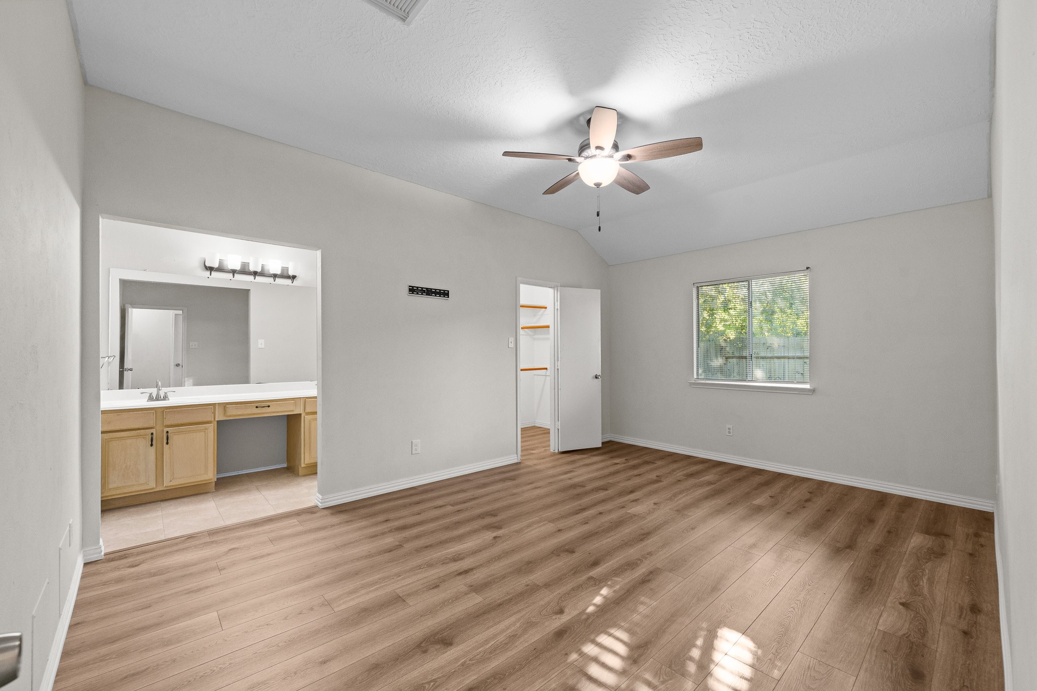 Spacious bedroom, abundant natural light from a window, and an attached bathroom with dual sinks and ample countertop space.