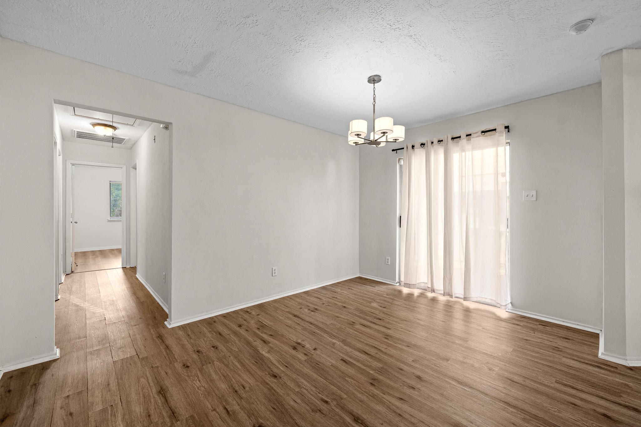 Bright dining area with, modern lighting, and sheer curtains allowing natural light to flow in.