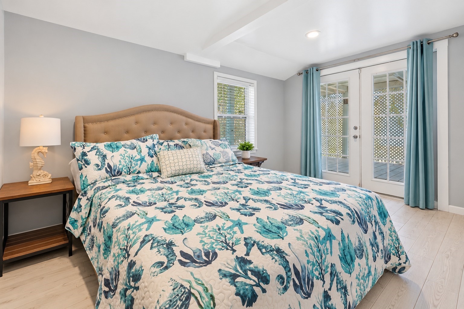 Spacious first downstairs bedroom featuring coastal-inspired dcor, abundant natural light, and French doors providing direct access to the covered outdoor area.