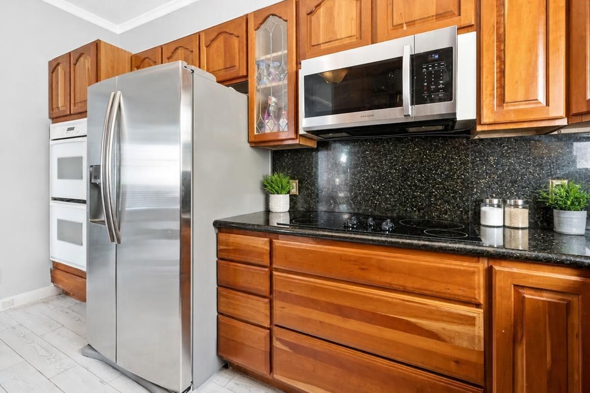 Additional view of the well-appointed second-floor kitchen, featuring rich wood cabinetry, sleek black granite countertops and backsplash, stainless steel appliances, a smooth-top electric cooktop, built-in microwave, and double ovens. With plenty of storage and convenient meal-preparation space, this inviting kitchen is ready for everything from quick beach-day breakfasts to memorable dinners with family and vacation guests!