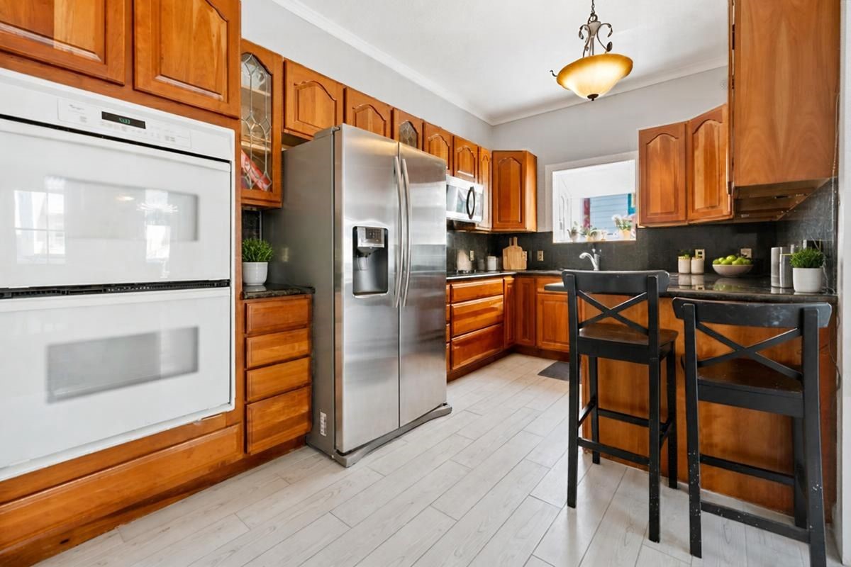 Second-Floor Kitchen: Welcome to the inviting second-floor kitchen, featuring warm wood cabinetry, generous counter space, a breakfast bar with seating for two, stainless steel refrigerator, built-in double ovens, and wood-look tile flooring. A charming space for preparing meals, gathering with family and friends, and enjoying the relaxed Galveston Island lifestyle after a day at the beach!
