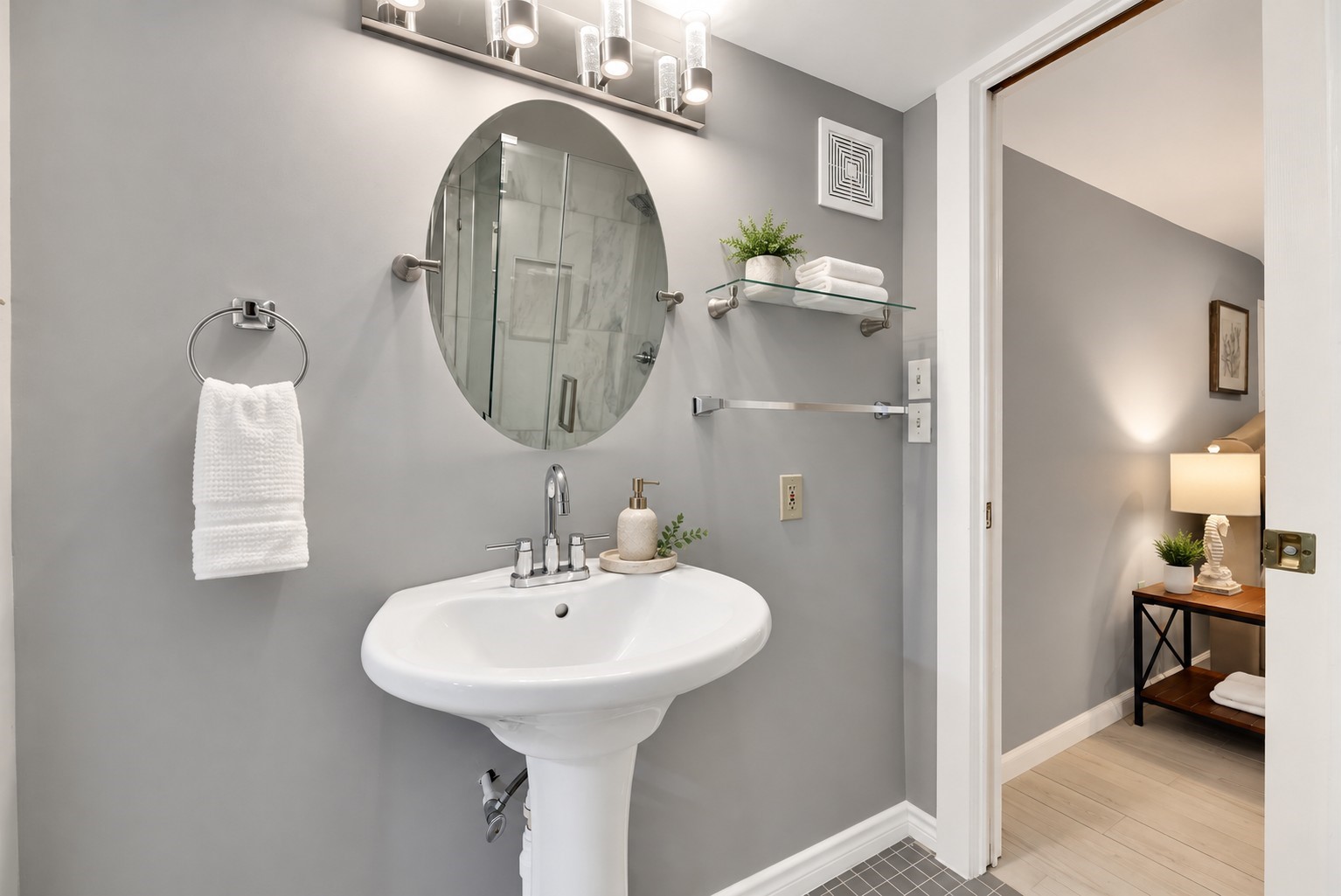 Additional view of the updated first-floor Jack-and-Jill bathroom shared by Bedrooms 1 and 2. Features a pedestal sink, stylish oval mirror, modern vanity lighting, contemporary fixtures, and neutral gray finishes, creating a clean and inviting coastal feel.