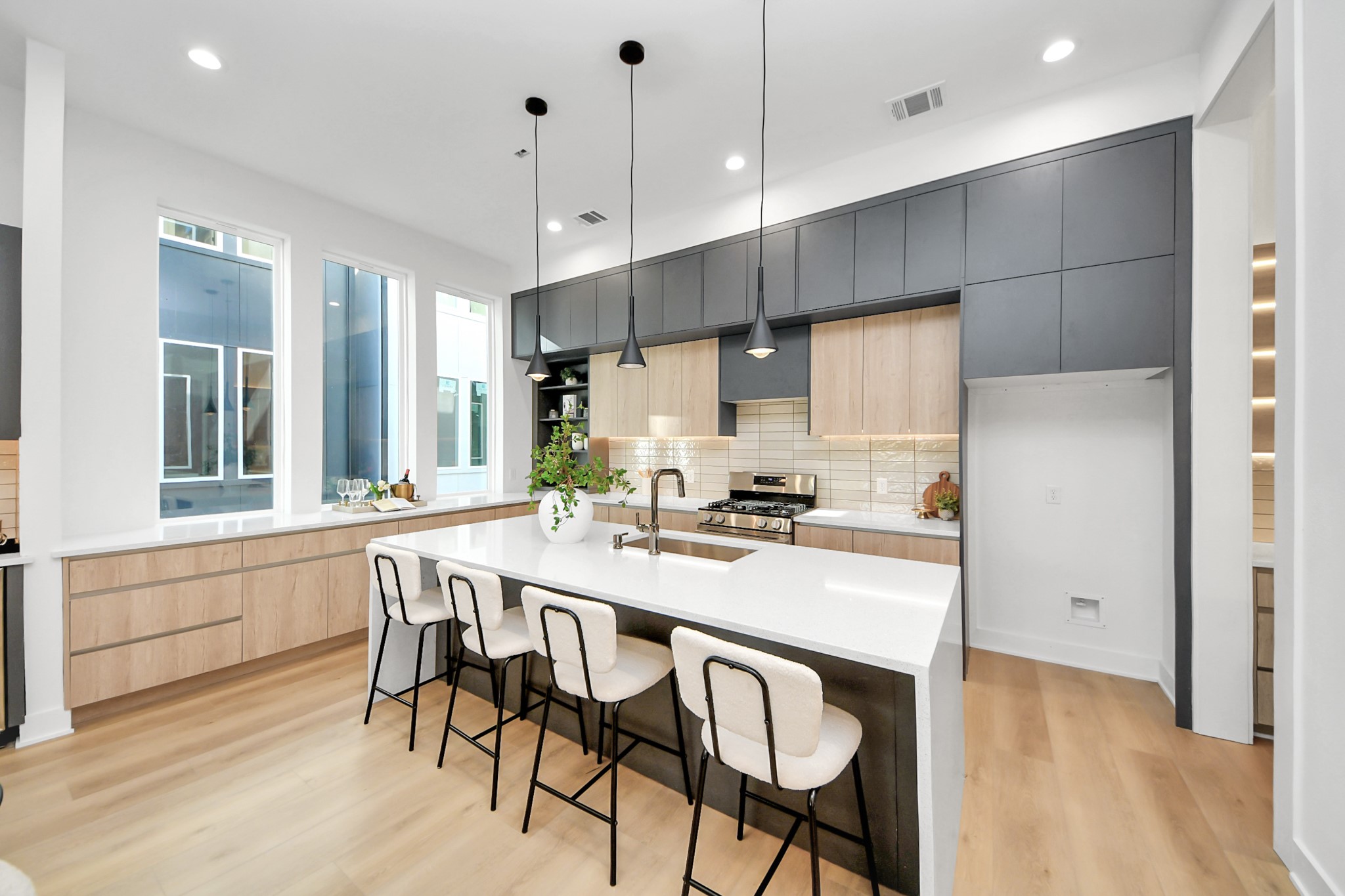 Modern kitchen featuring a spacious waterfall island, pendant lighting, two-tone cabinetry, and stainless steel appliances.