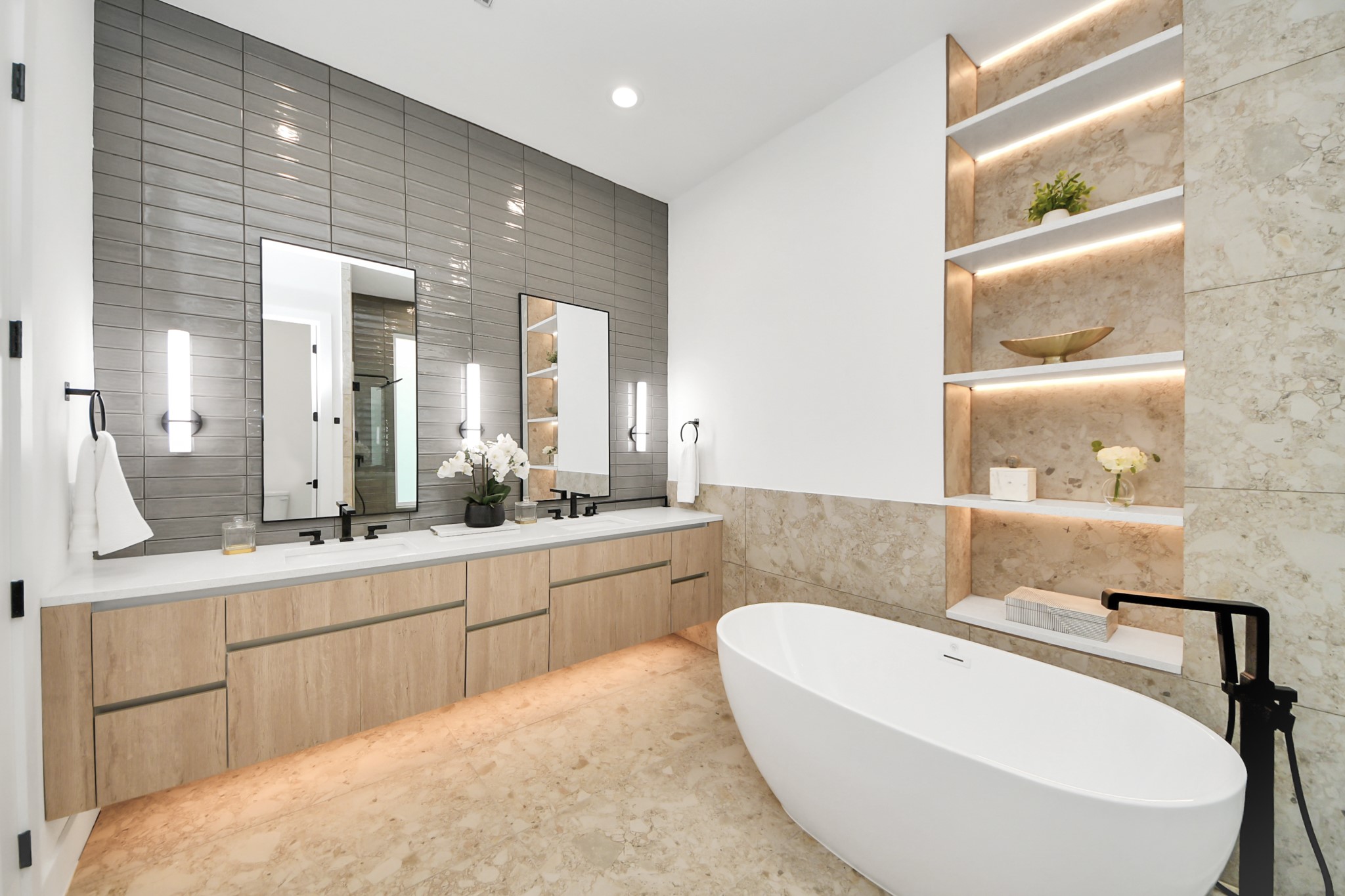 Primary bathroom featuring a double vanity, freestanding tub, and contemporary tilework.