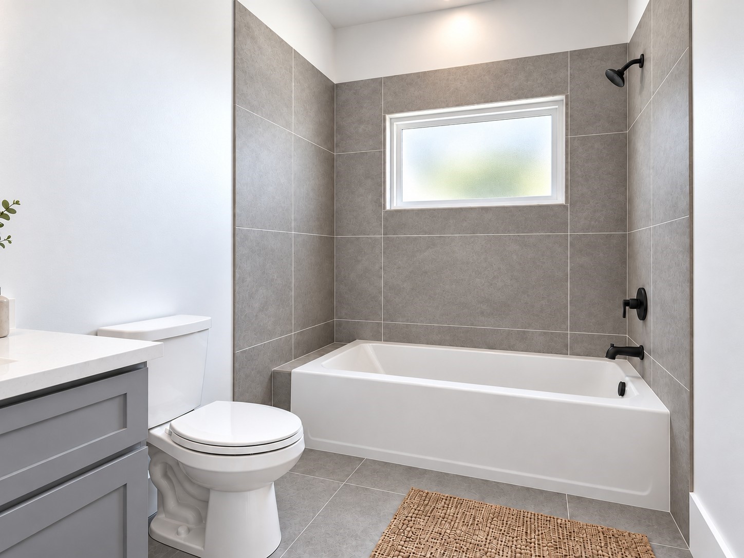 This bright and beautifully finished bathroom offers a perfect balance of comfort and contemporary style. A spacious bathtub is surrounded by elegant textured gray tile, creating a sophisticated focal point. A frosted window above the tub allows natural light to enter while maintaining privacy. Matte black shower and bath fixtures provide a striking contrast against the neutral finishes. These photos have been virtually rendered for visual reference.