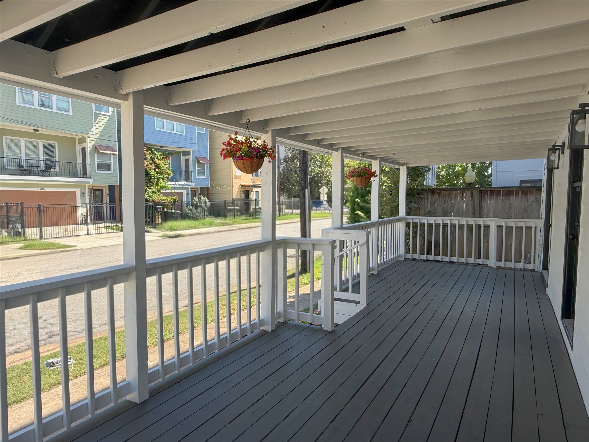Generously sized outdoor living space featuring painted wood decking, exposed ceiling beams, and hanging flower baskets.