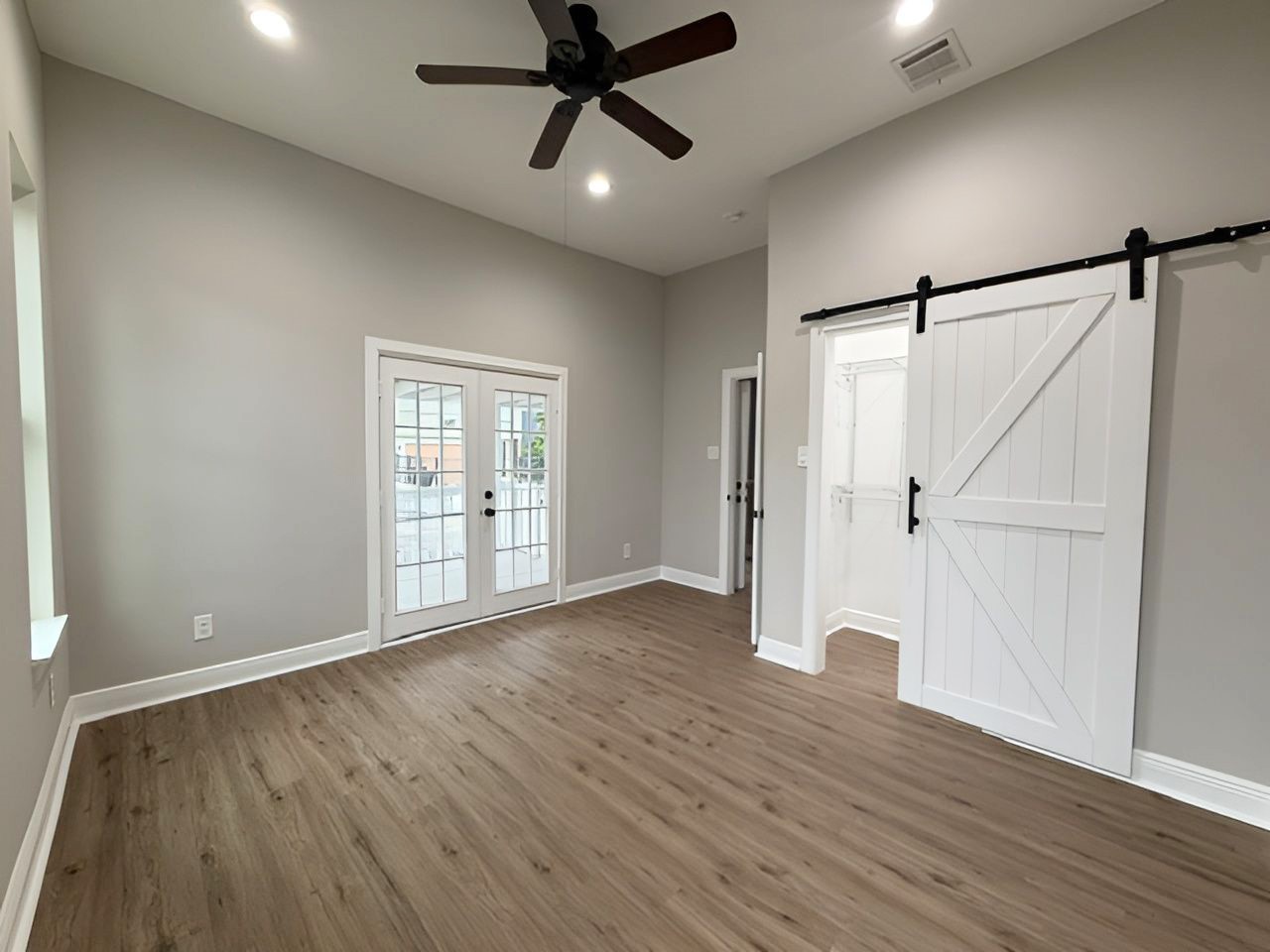 This angle showcases the sliding barn door closet, attractive flooring, and spacious layout, with French doors providing additional natural light.