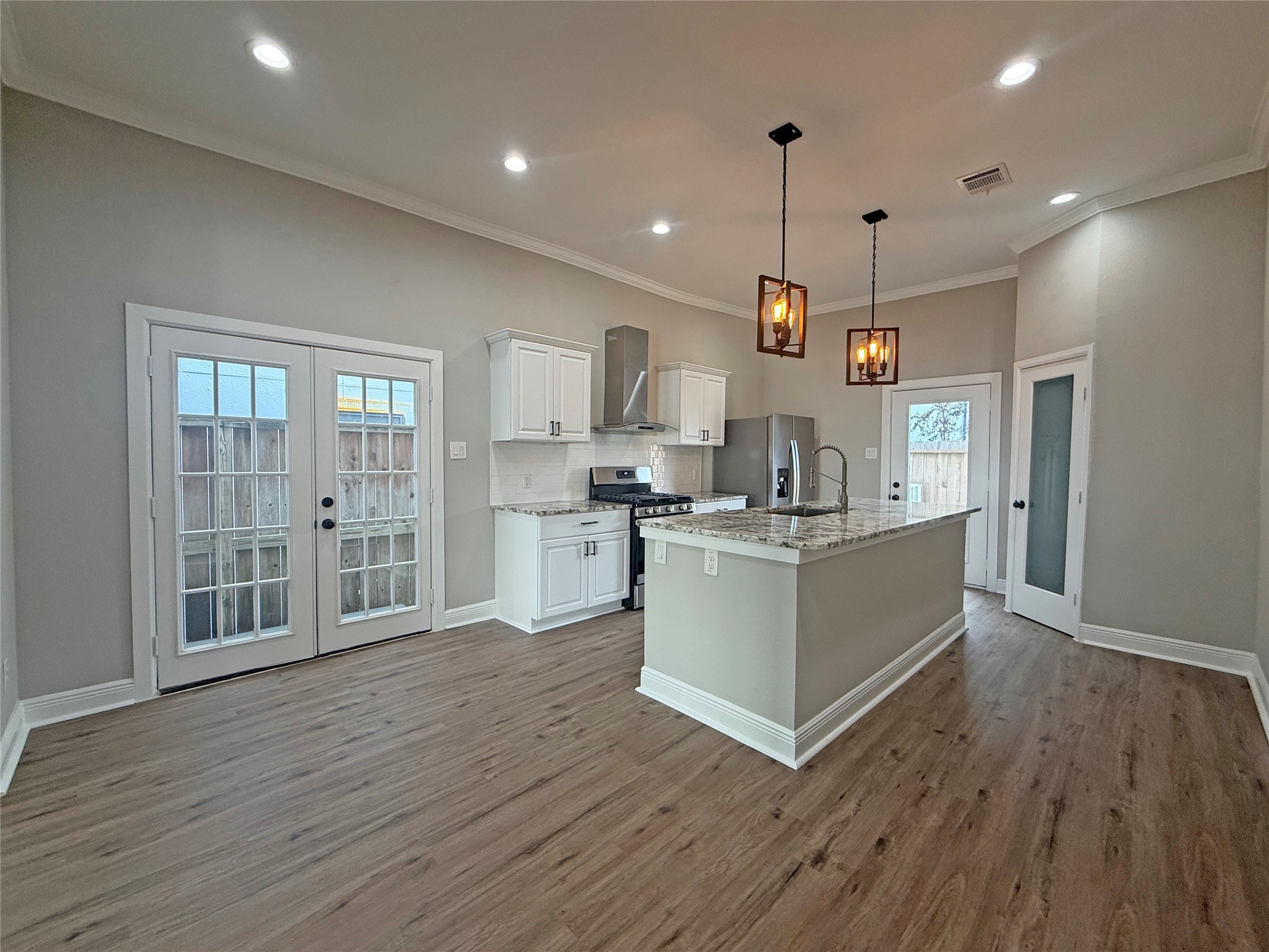 Open-concept kitchen features white cabinetry, granite countertops, stainless steel appliances, and stylish pendant lighting. French doors off the dining area and a separate exterior door near the kitchen provide convenient outdoor access.