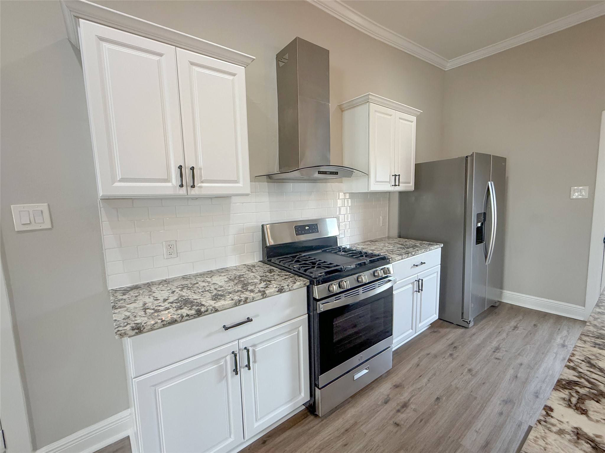 Beautifully appointed kitchen featuring white shaker-style cabinetry, granite countertops, subway tile backsplash, NEW stainless steel gas range, coordinating vent hood, and refrigerator.