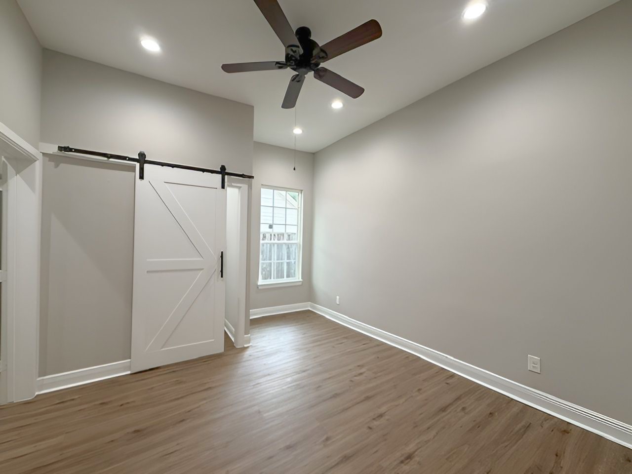 Spacious primary bedroom features high ceilings, recessed lighting, a ceiling fan, and a charming sitting area nestled beside the window. A sliding barn door adds a distinctive touch.