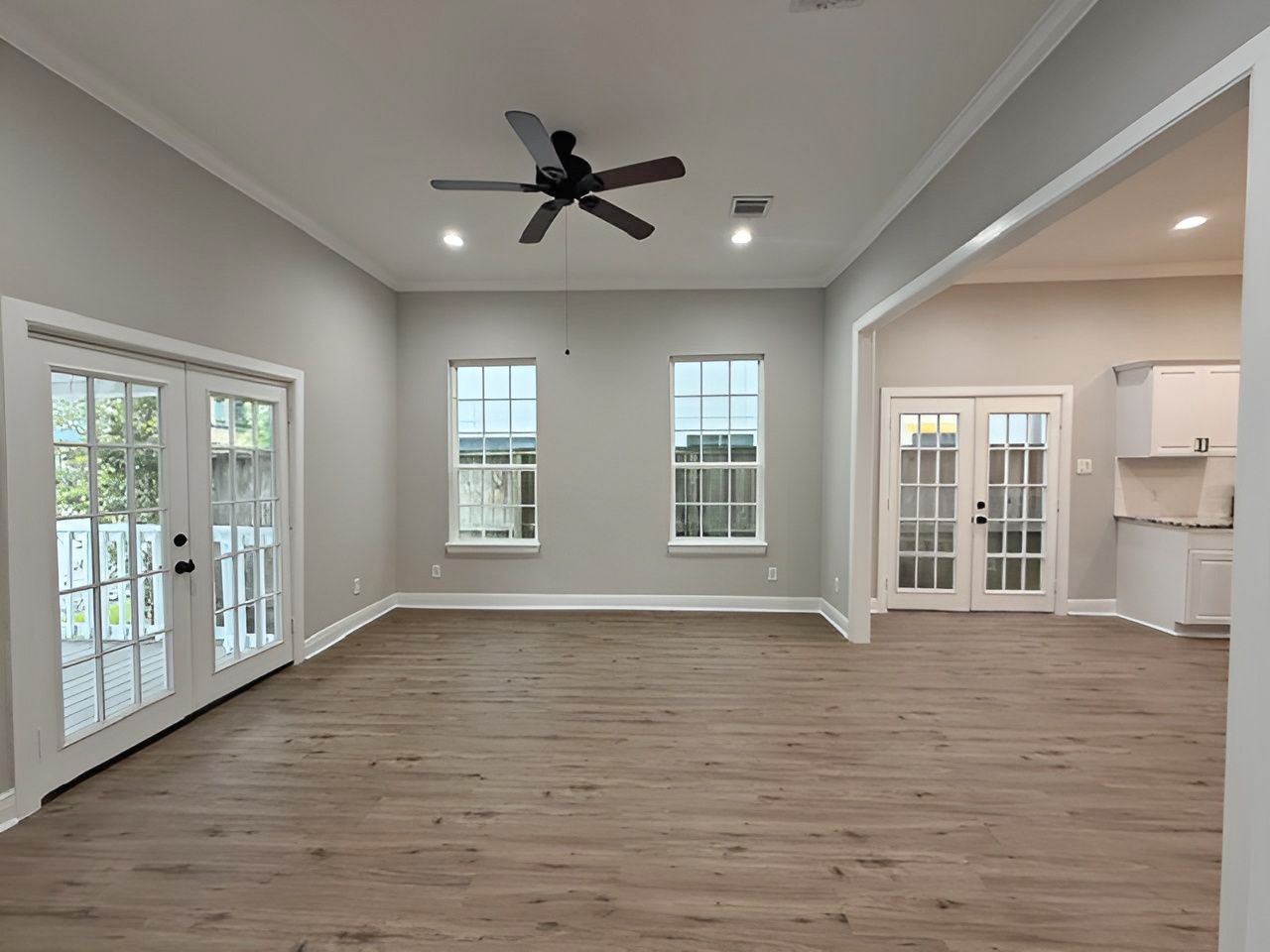 Bright, open living space featuring updated wood-look flooring, NEW paint, recessed lighting, crown molding, and a ceiling fan offering flexibility for a variety of furniture arrangements.