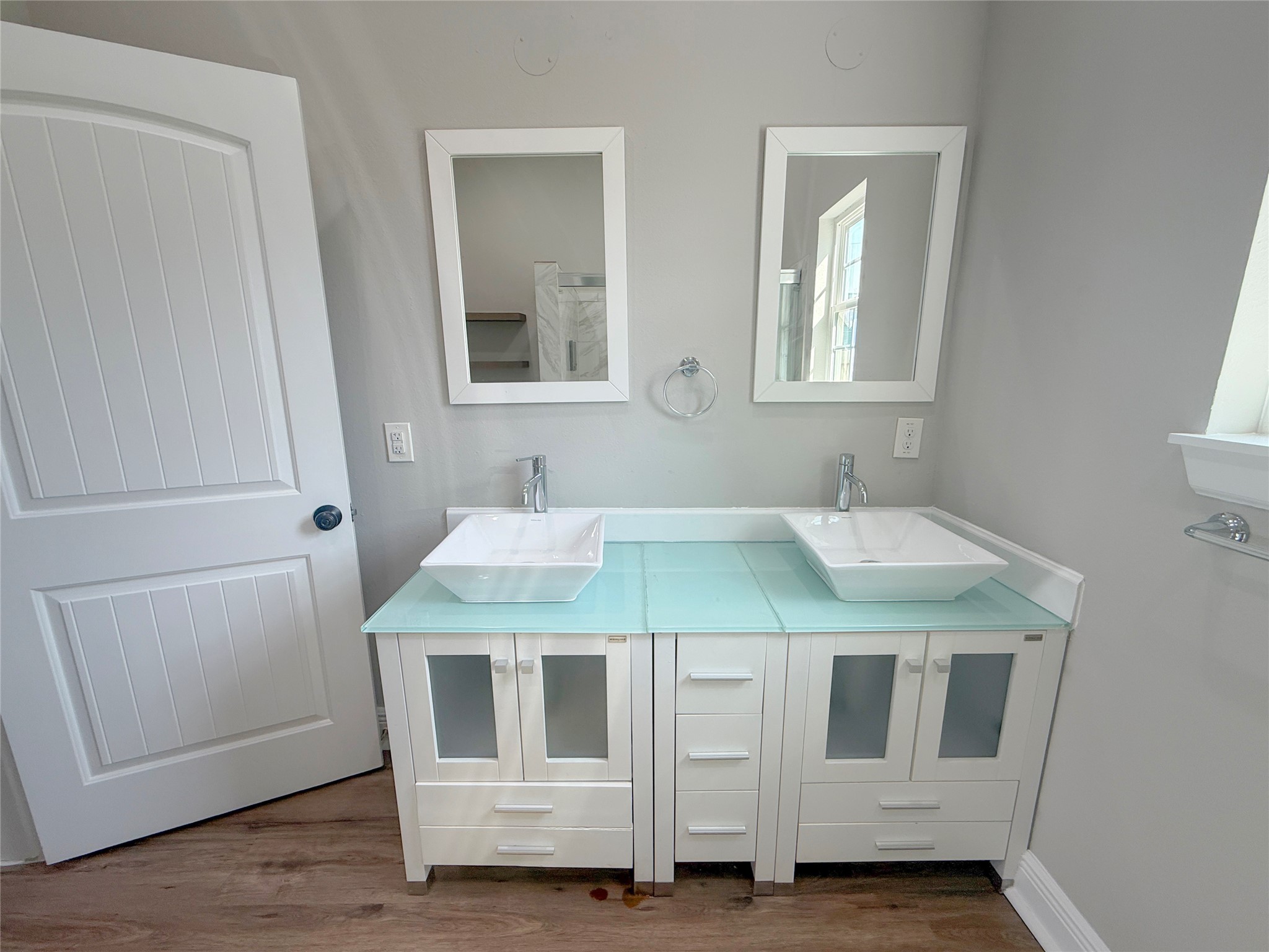 Contemporary double-sink vanity features vessel sinks, sleek faucets, glass countertops, individual mirrors, and generous cabinet storage.