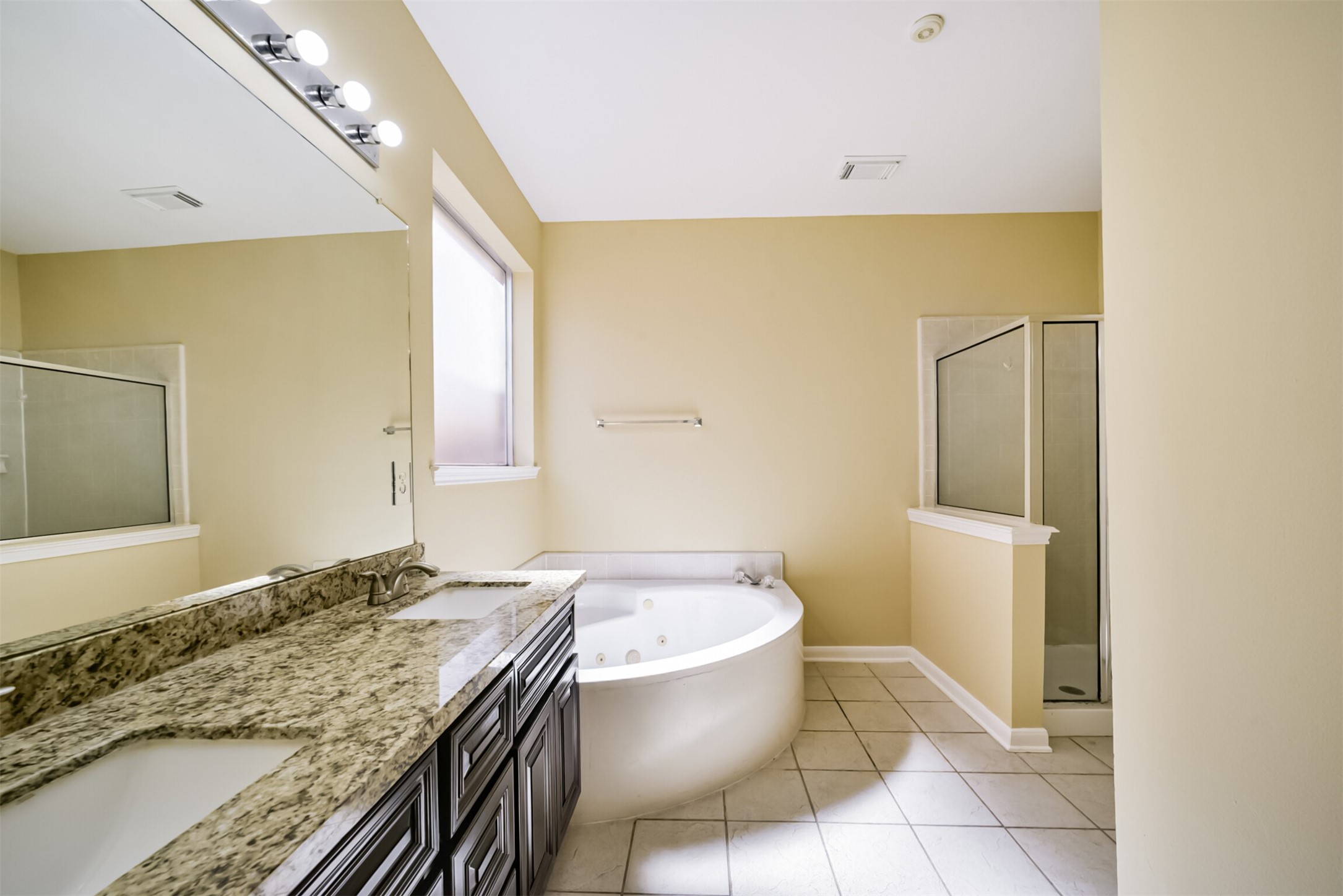 Primary ensuite featuring a jetted tub, walk-in shower, and frosted window for natural light with privacy.