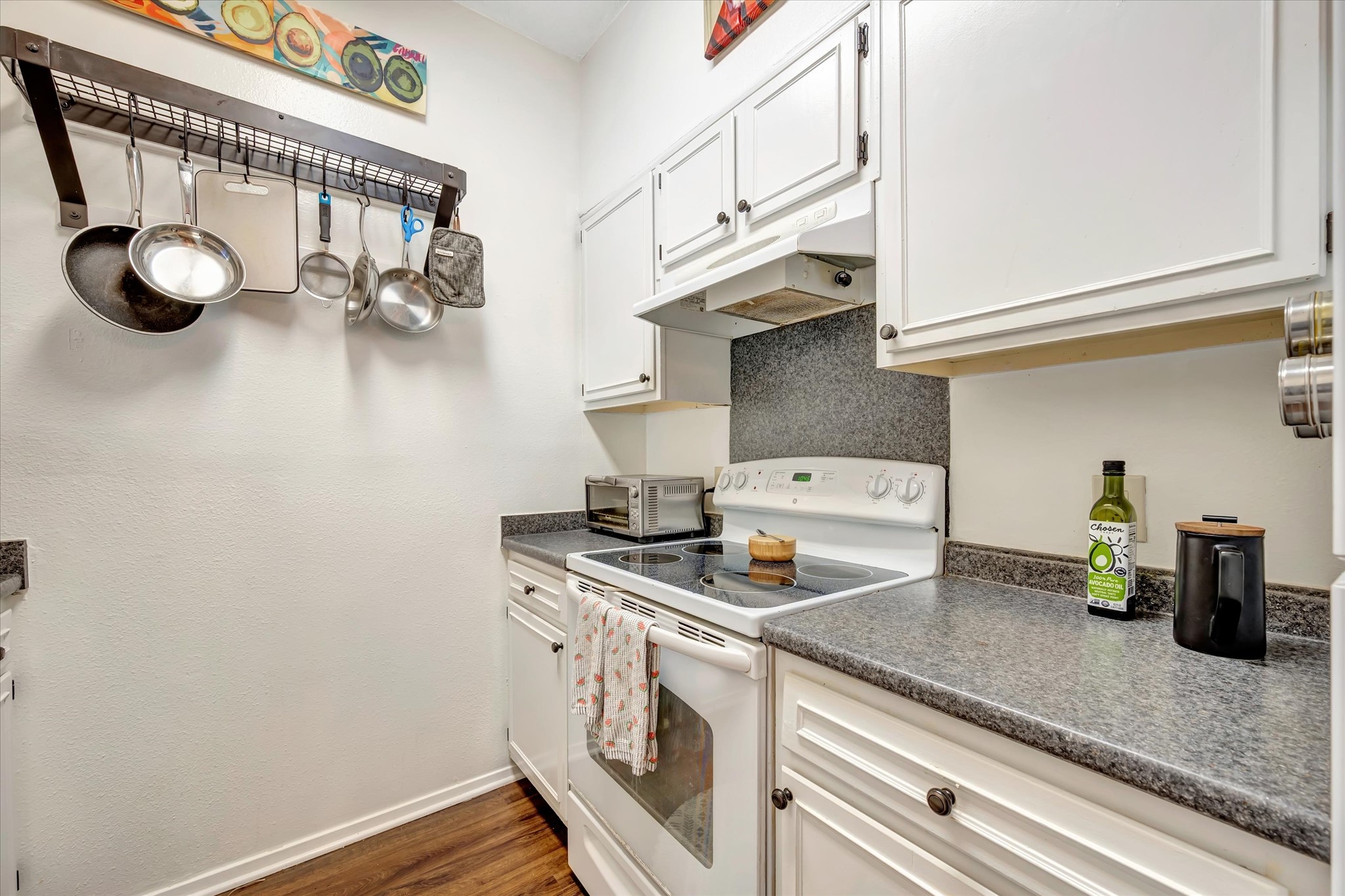 Kitchen cooking area with a range, vent hood and surrounding cabinet storage.