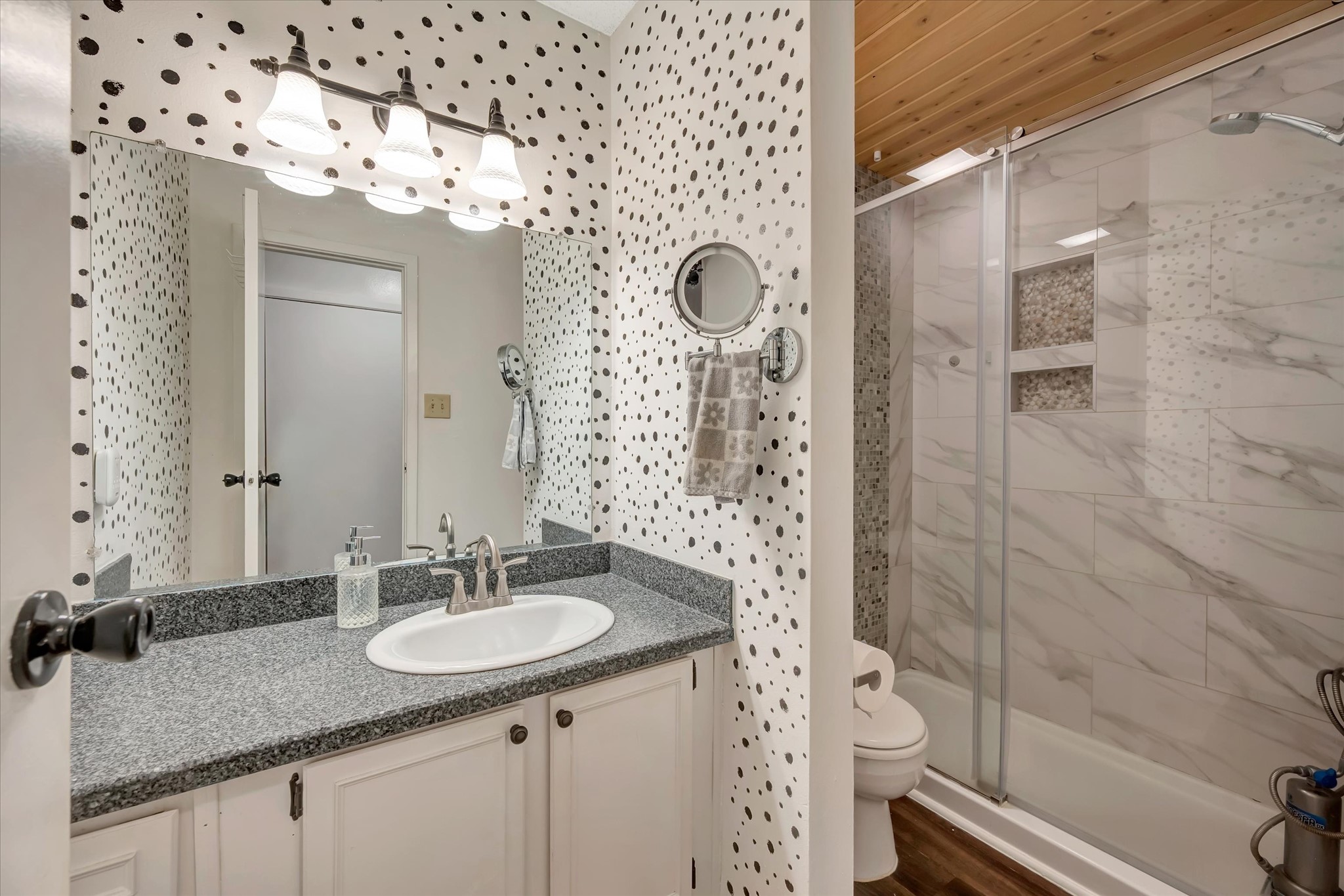 Bathroom with a vanity, patterned wall detail and a glass-enclosed shower.