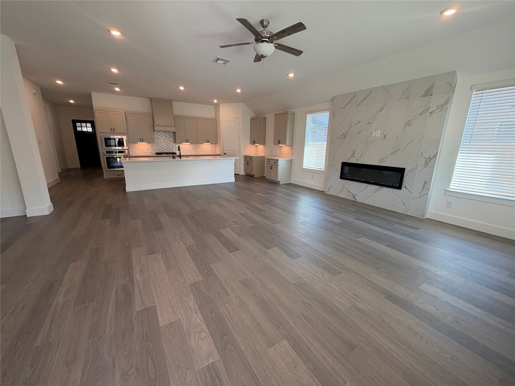 Spacious open-concept living area featuring sleek hardwood floors, a modern kitchen with a large island, and a stylish fireplace set against a chic tiled wall.