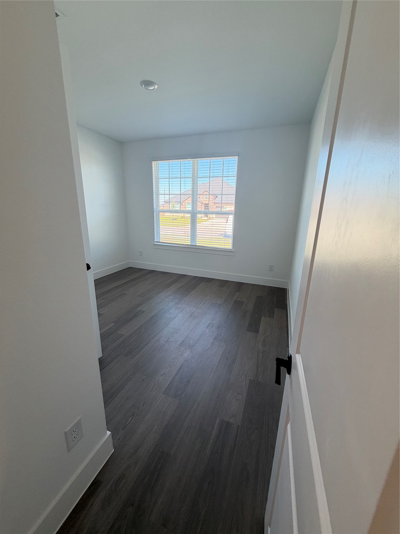 Bright and inviting bedroom featuring sleek dark wood flooring and a large window offering ample natural light.