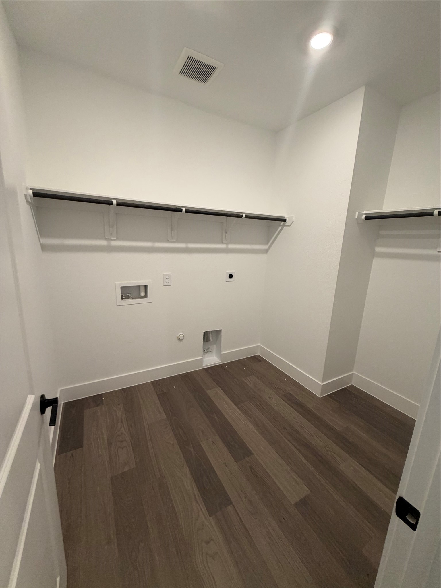 Spacious laundry room with sleek hardwood flooring, ample shelving, and hookups for washer and dryer.