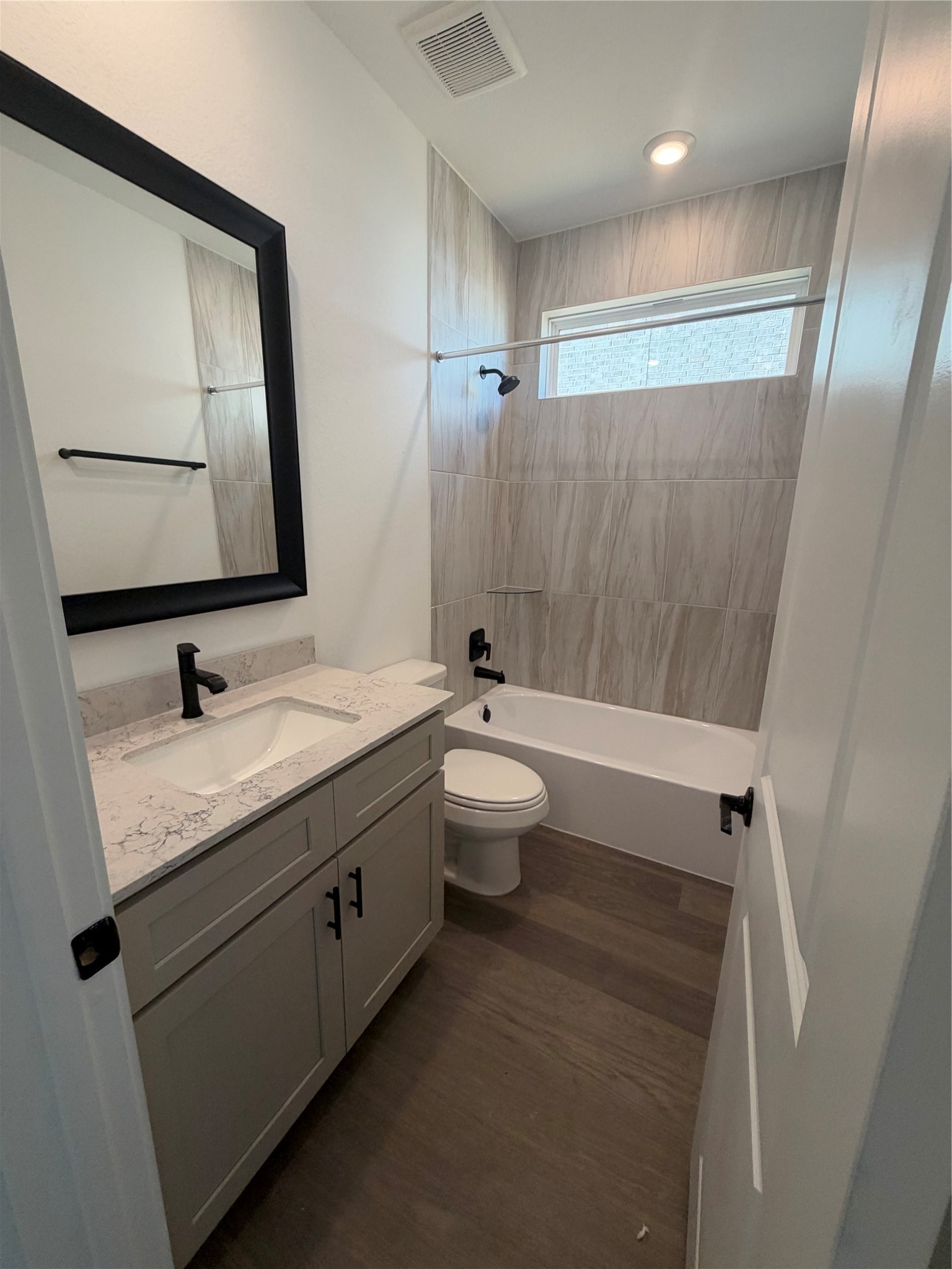 Stylish bathroom featuring a modern vanity with a sleek black framed mirror, elegant marble countertop, and a sophisticated tub with contemporary tile surround.