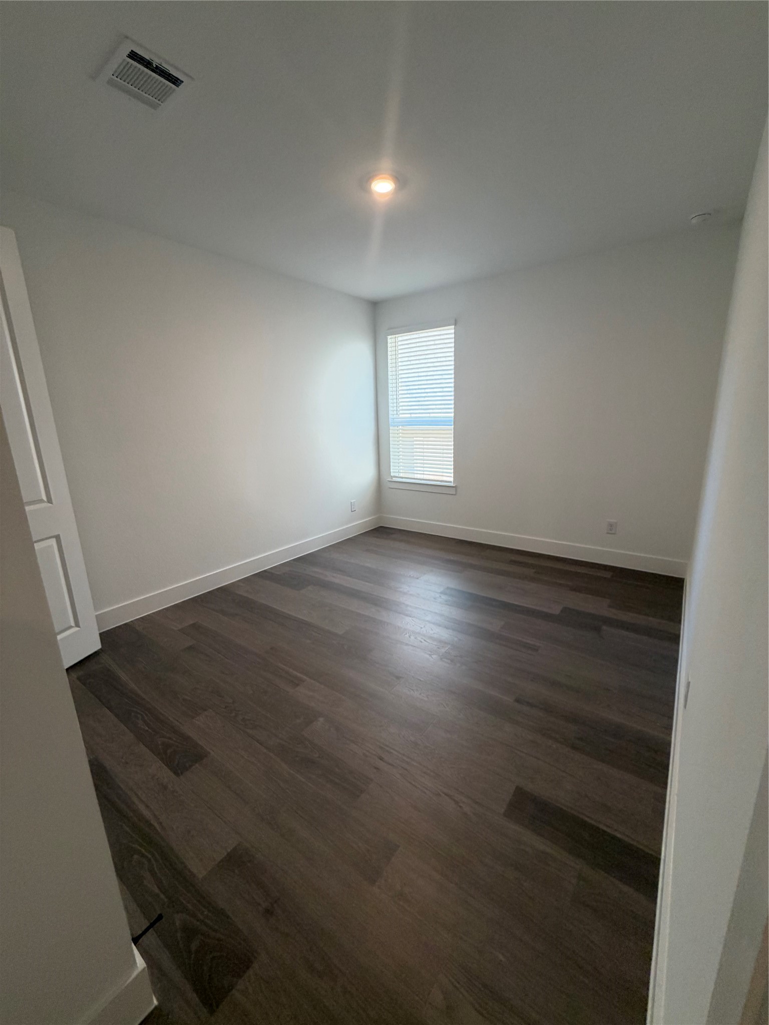 Bright, minimalist bedroom with sleek dark hardwood floors and a large window for natural light.