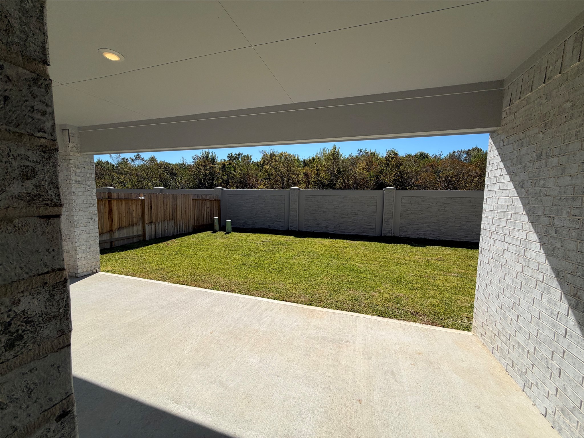 Spacious covered patio overlooking a private, fenced backyard with lush green lawn, perfect for outdoor activities and relaxation.