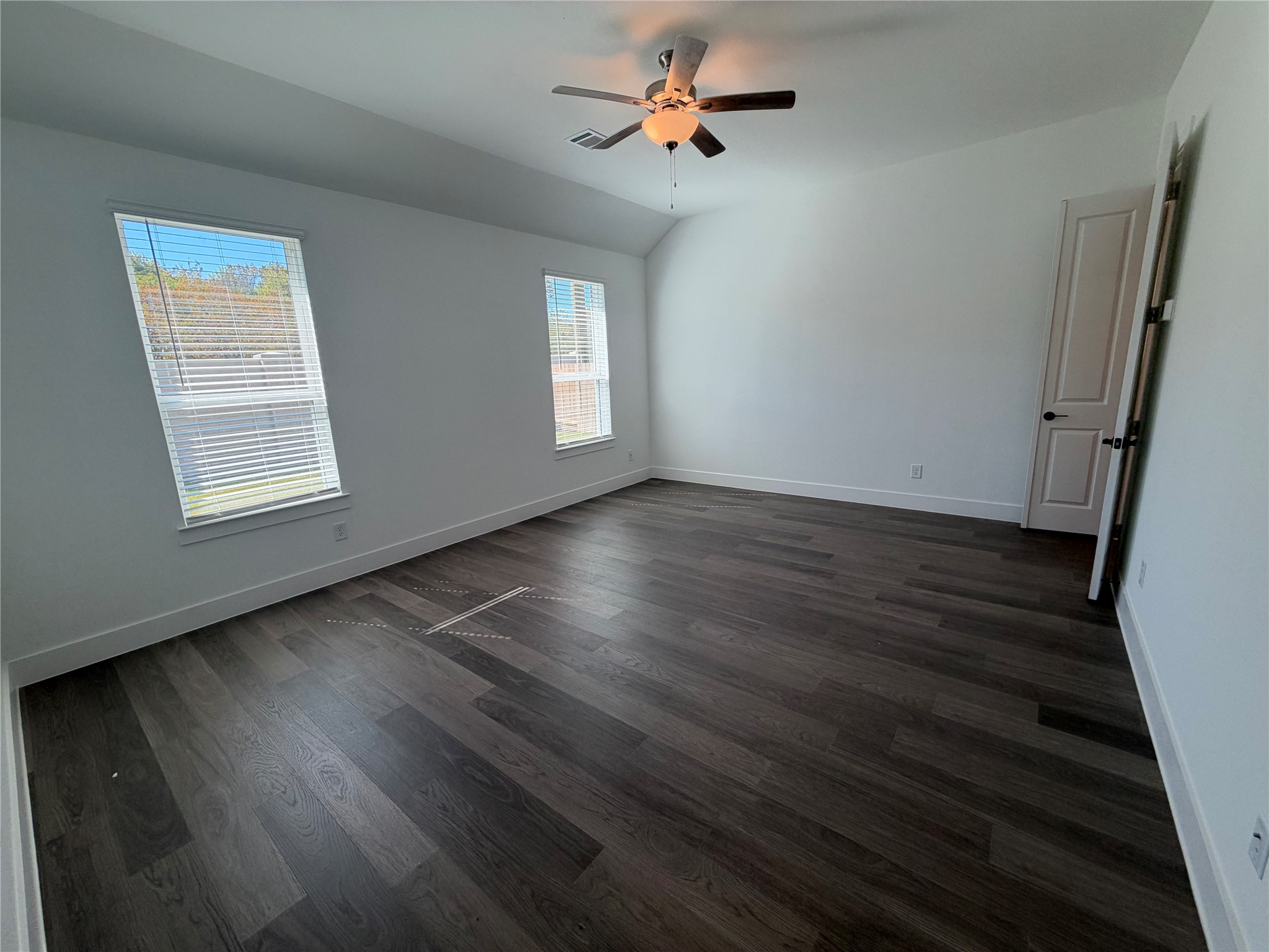 Spacious primary bedroom featuring rich, dark wood flooring, large windows for natural light, and a ceiling fan for comfort.