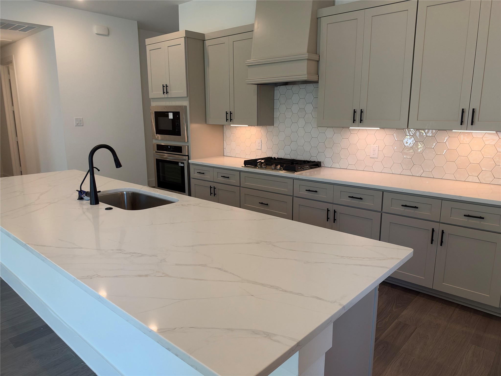 Modern kitchen featuring sleek gray cabinetry, a spacious marble island with a built-in sink, and a stylish hexagonal tile backsplash, perfect for culinary enthusiasts.