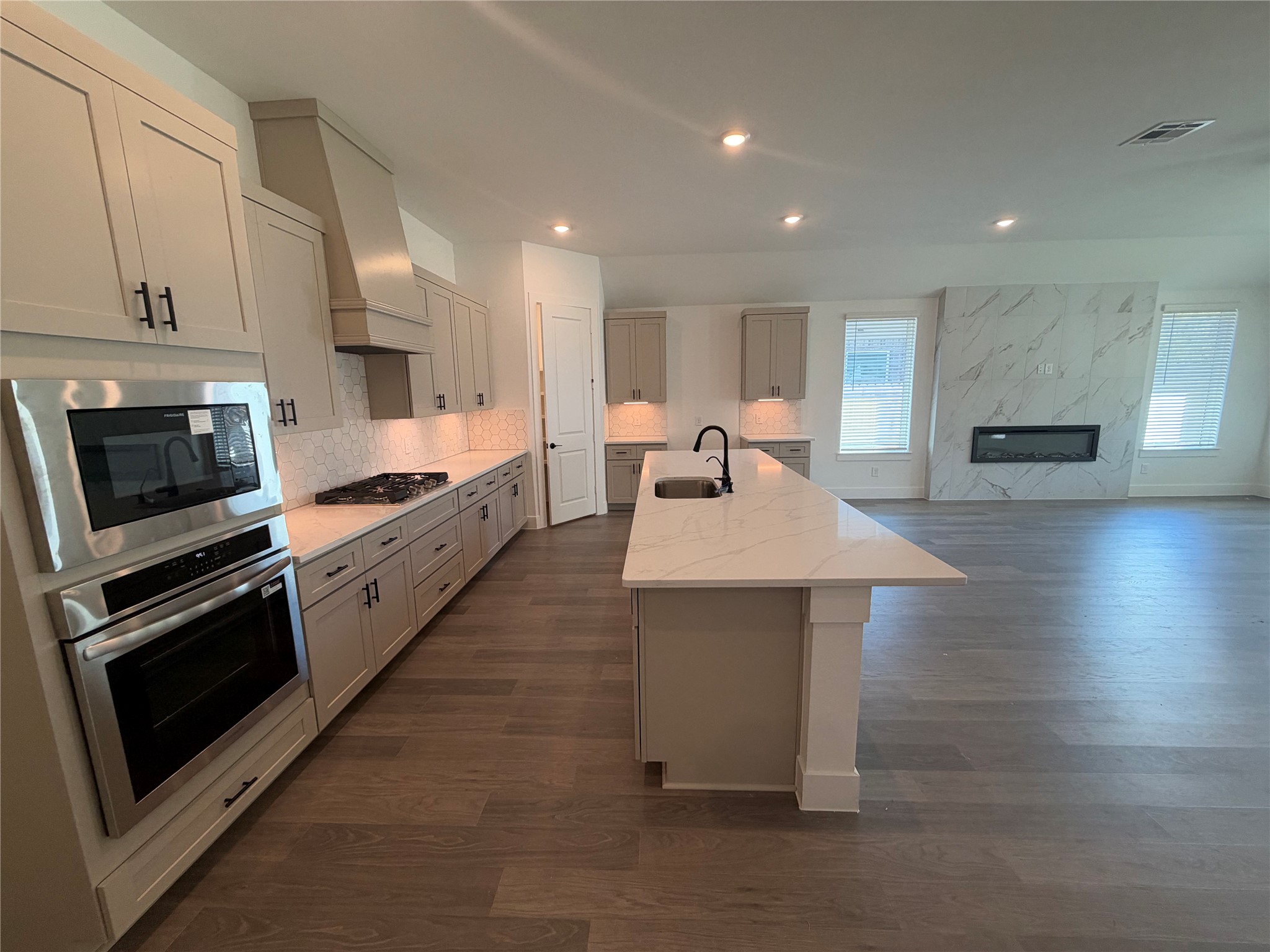 Spacious modern kitchen with sleek cabinetry, stainless steel appliances, and a large island, seamlessly flowing into an open living area featuring a stylish fireplace.