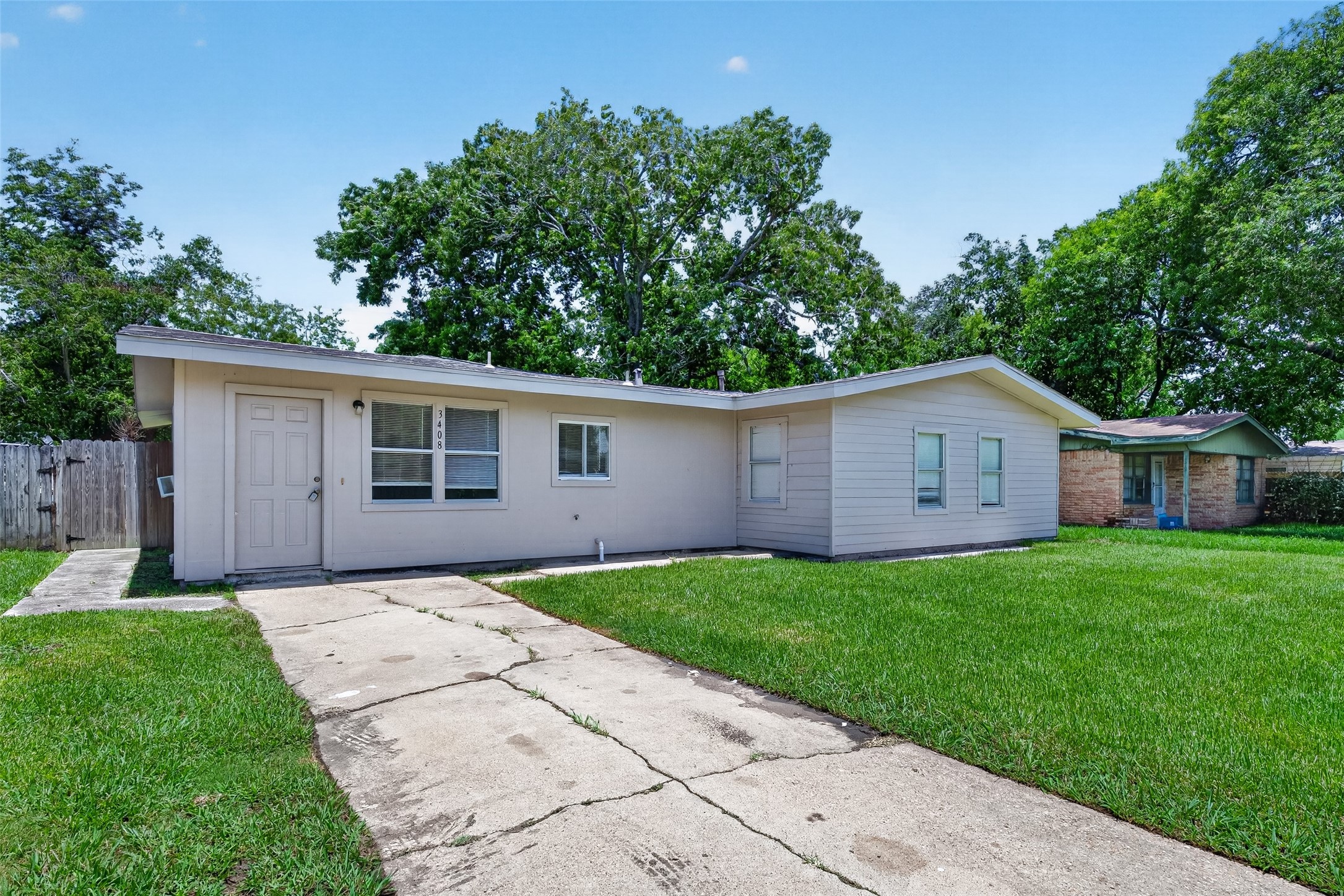 Discover this charming single-story home featuring a light facade, inviting front porch, and ample windows. Nestled on a grassy lot with a paved driveway, it offers privacy and shade from mature trees.