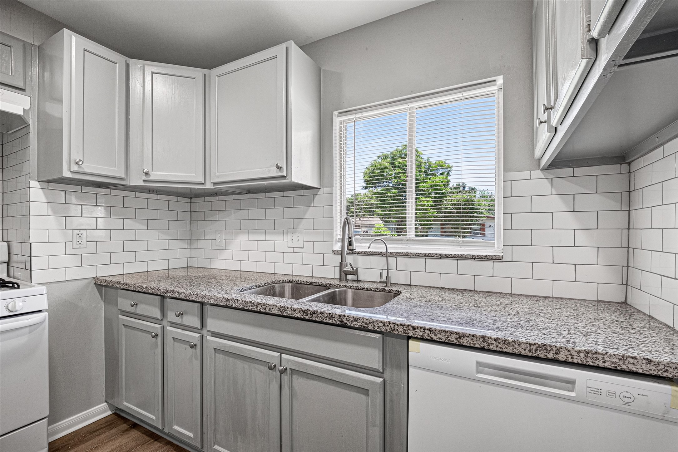 This kitchen features sleek granite countertops, white cabinetry, and a modern subway tile backsplash. It includes a double sink, dishwasher, and a window with a view, offering a bright and functional space.