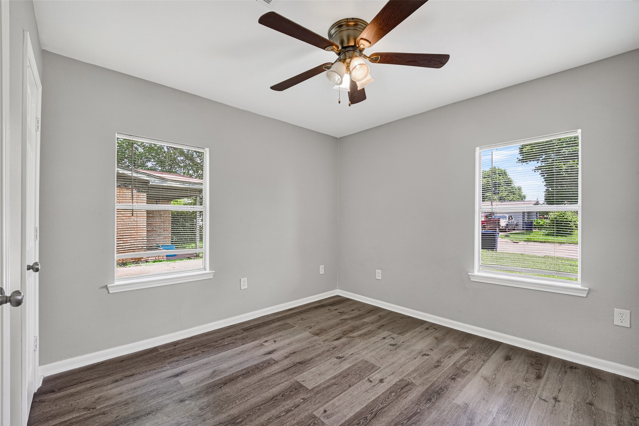 This room features two large windows for natural light, fresh gray walls, modern wood flooring, and a ceiling fan, creating a bright and inviting space.
