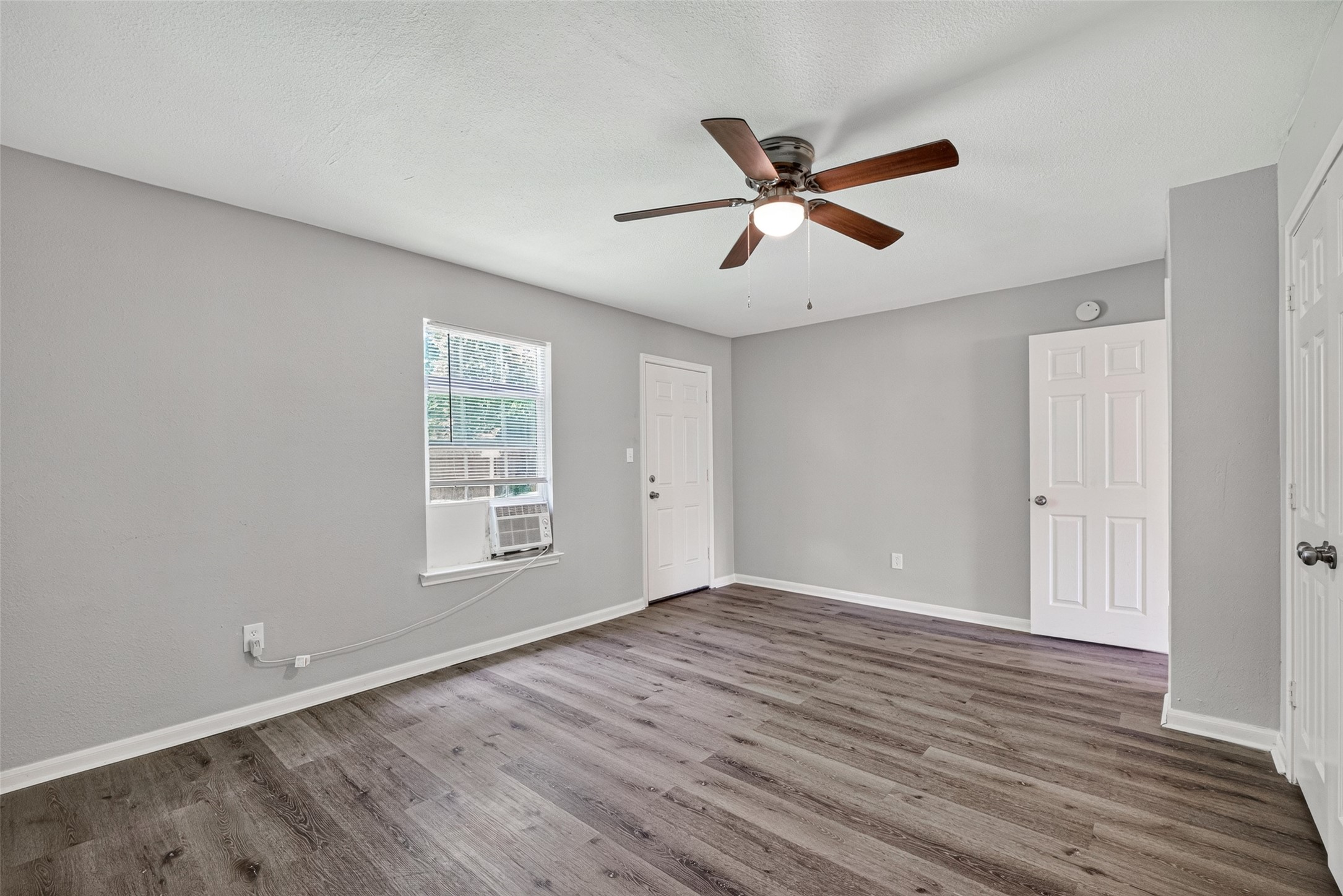 This inviting room boasts a chic gray palette, wood-style flooring, and a ceiling fan. Enjoy abundant natural light and comfort from the window AC unit.