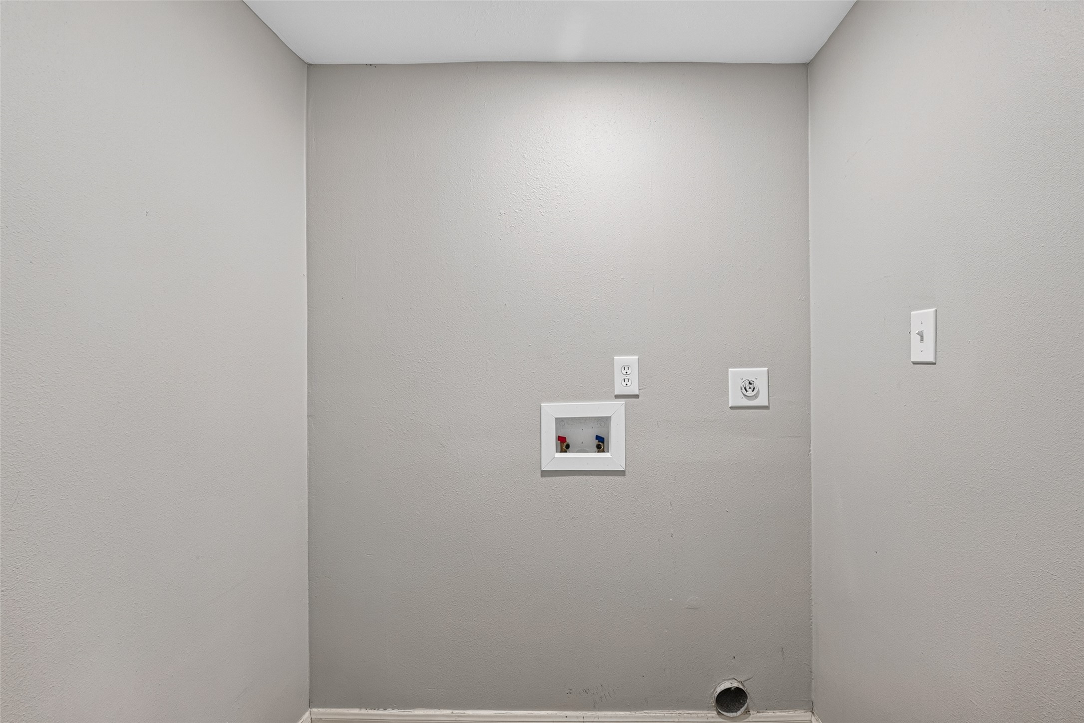 This image shows a utility area designed for laundry, featuring hookups for a washer and dryer on a plain, light-colored wall.