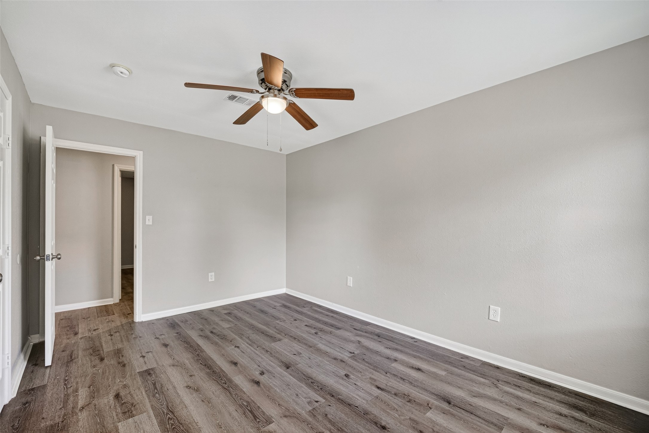 This room features freshly painted neutral walls, wood-look flooring, and a ceiling fan. It has a simple, clean design, ideal for a bedroom or office space.
