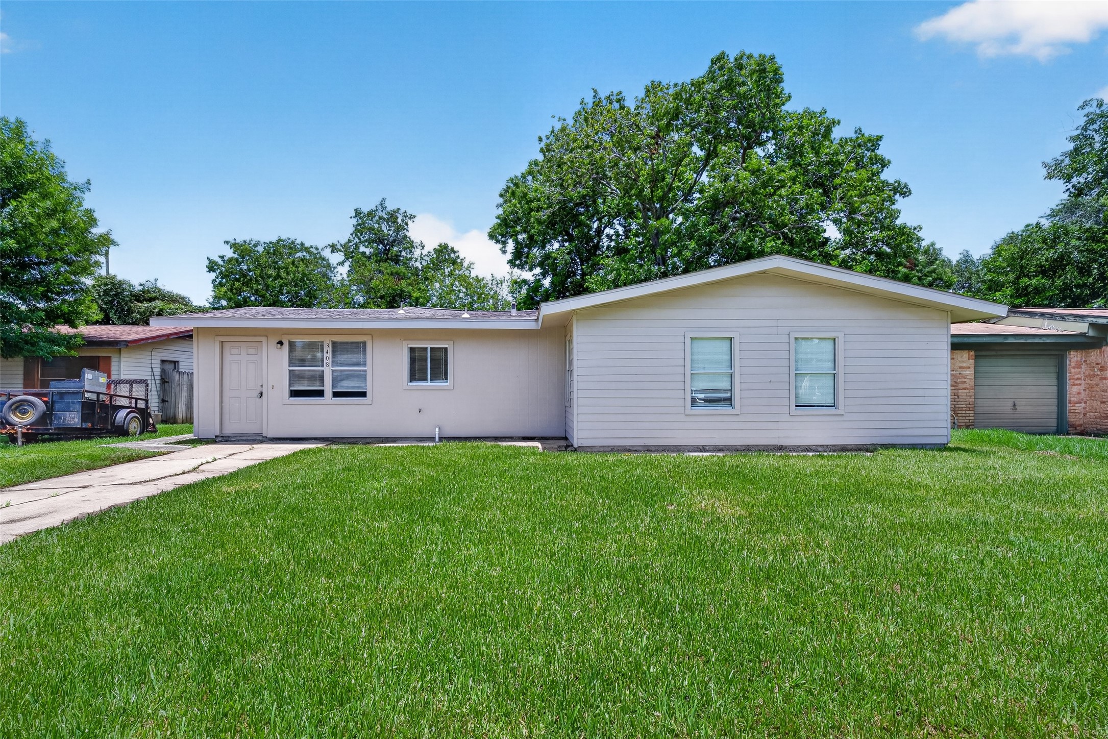 Charming single-story home with light siding and a pristine lawn. Enjoy a paved walkway to the entrance and the tranquility of mature trees providing natural shade.
