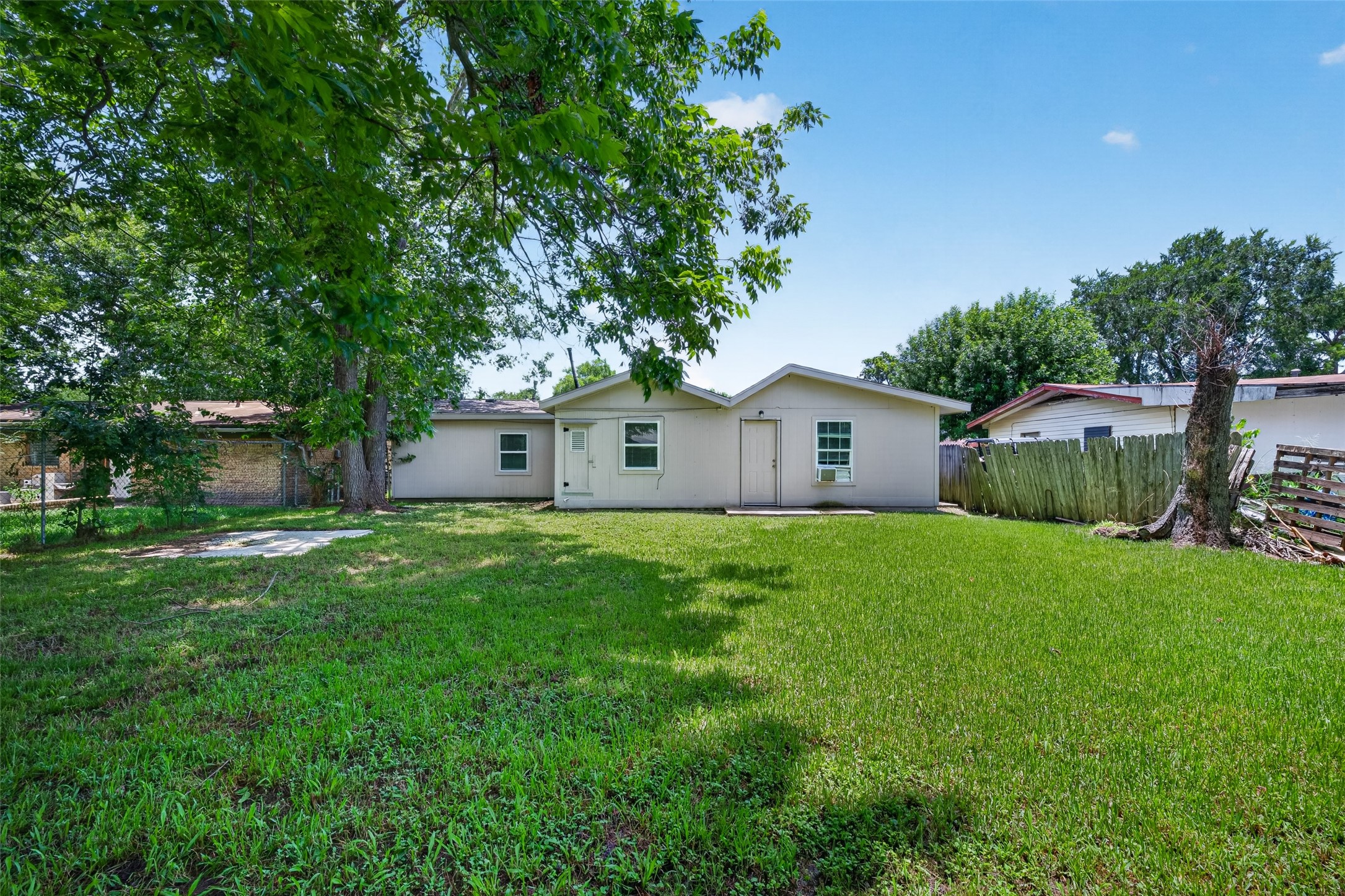 Charming backyard with lush grass, mature trees, and a cozy single-story house. Fenced for privacy, offering ample space for outdoor activities.