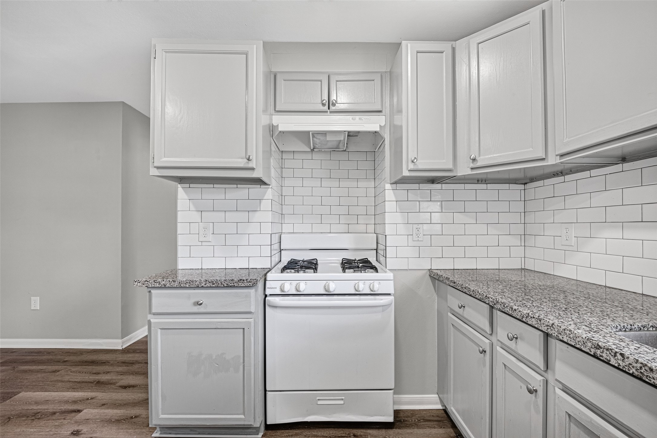 This kitchen features modern white cabinetry, a gas stove, and sleek granite countertops. The subway tile backsplash adds a classic touch, complementing the neutral color palette.