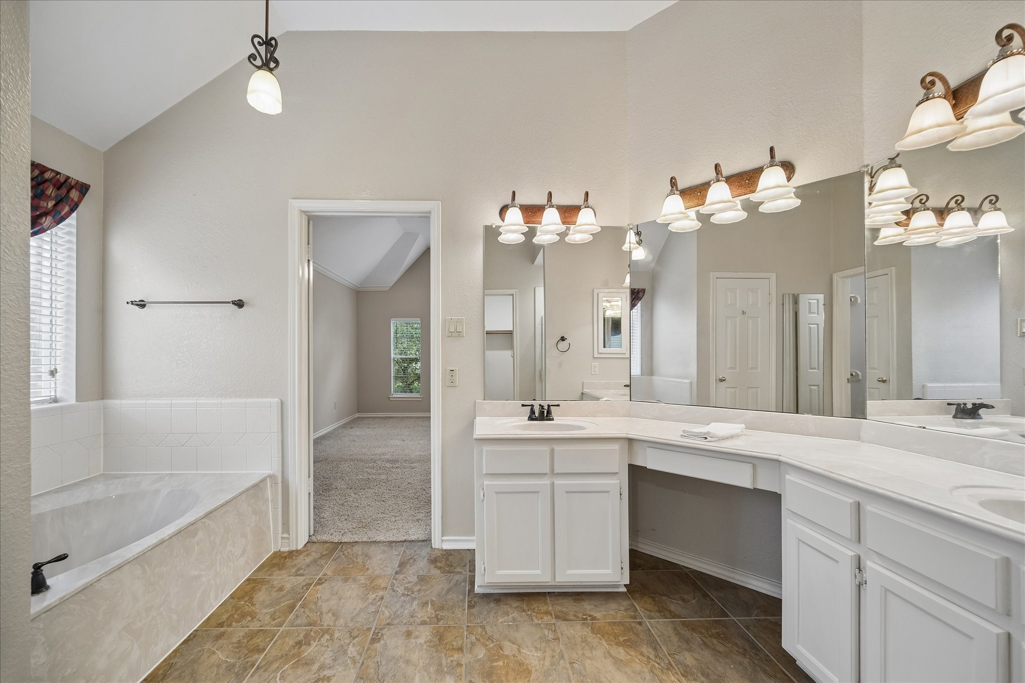 This view of the primary bathroom shows you the jetted tub on the left, doorway to the bedroom and the vanity area.  Behind are 2 walk-in closets.