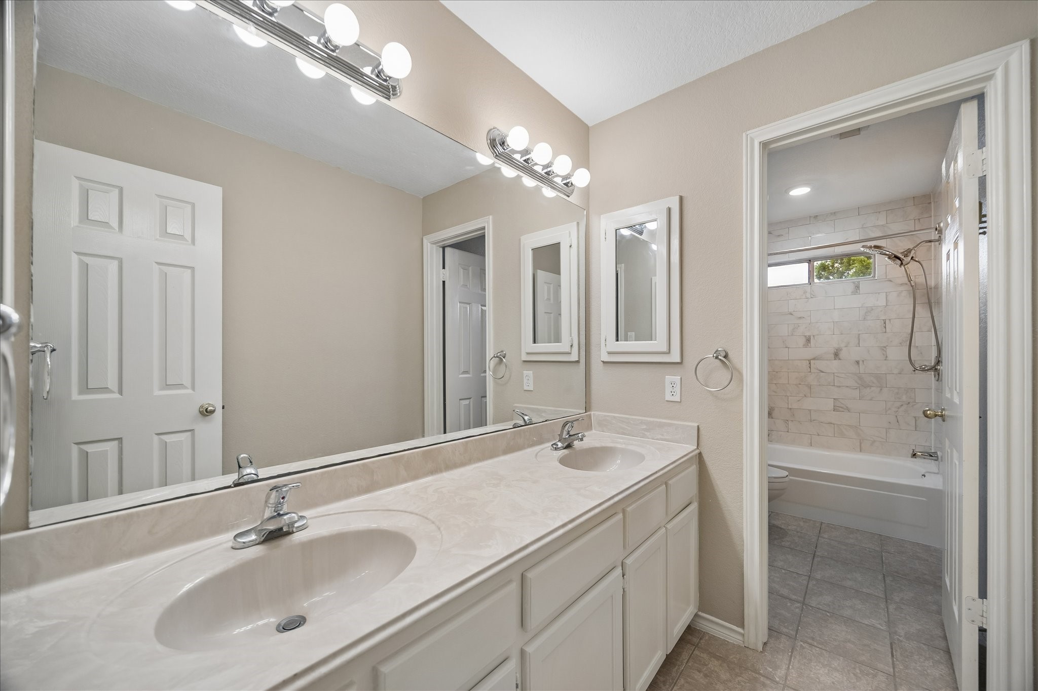 This is the secondary bathroom upstairs.  Dual sinks, lots of cabinets, including on through the door and on the left.  Beautiful tile tub with shower and small window above.