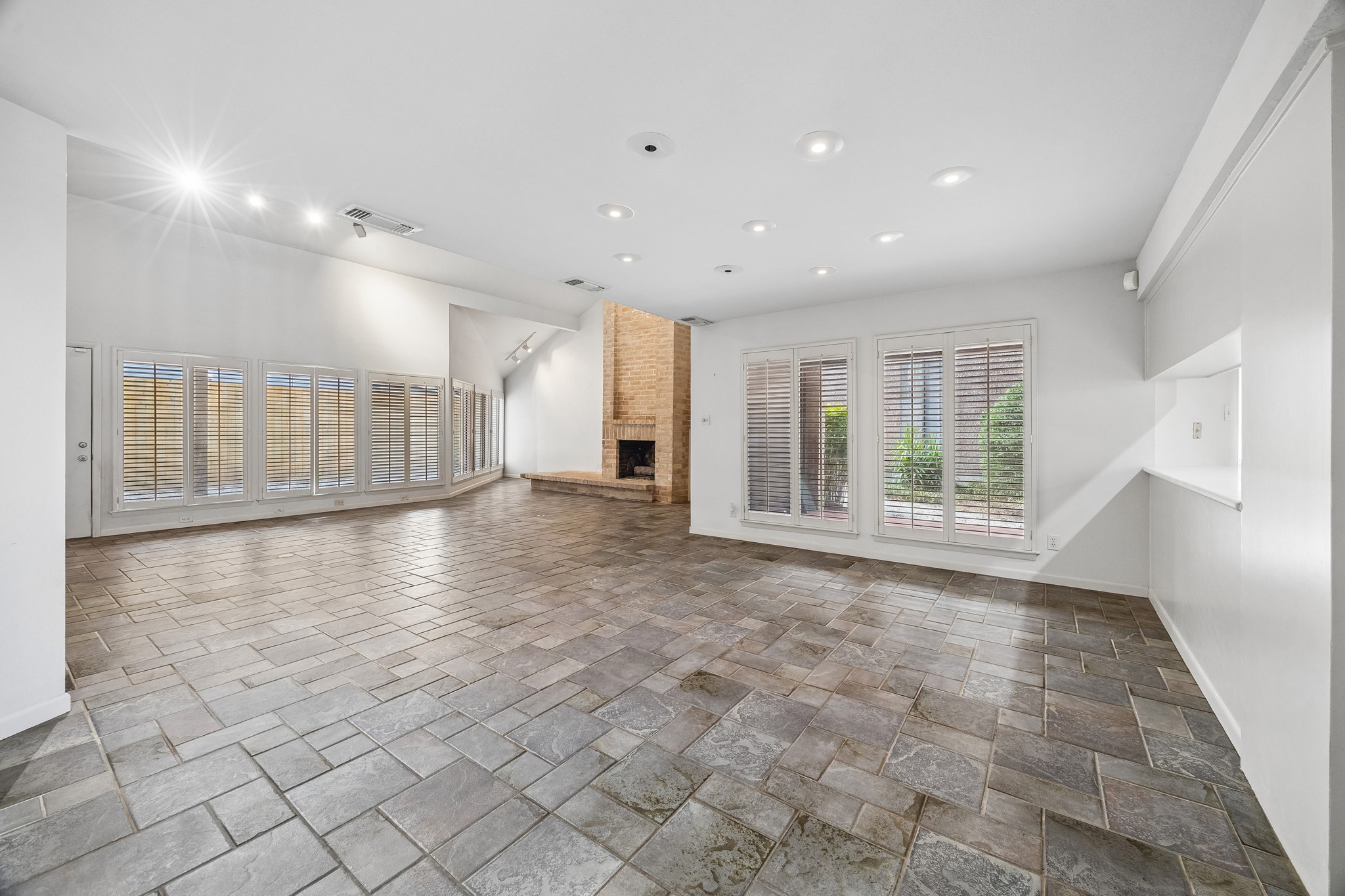 Large open floor plan with dining area open to kitchen and family room across the back of the home. The home features floor to ceiling windows and natural tile flooring.