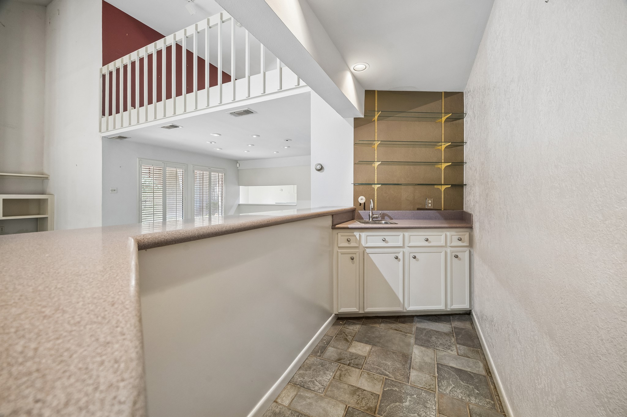 Behind the Bar is stainless bar sink, glass shelving and cabinets below.
